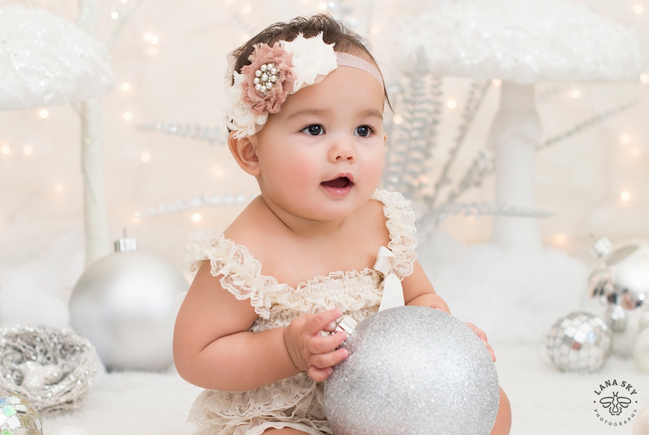 A holiday-themed photo of a toddler girl holding an over-sized ornament