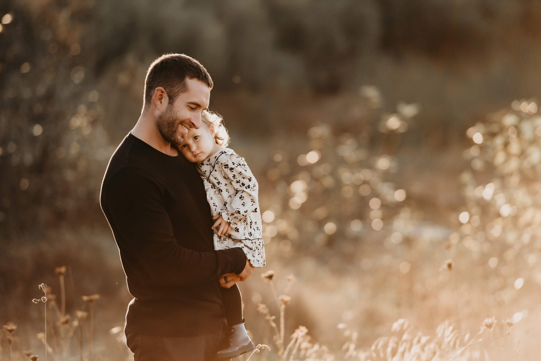 Dad lovingly holding his daughter in his arms, standing in a beautiful field