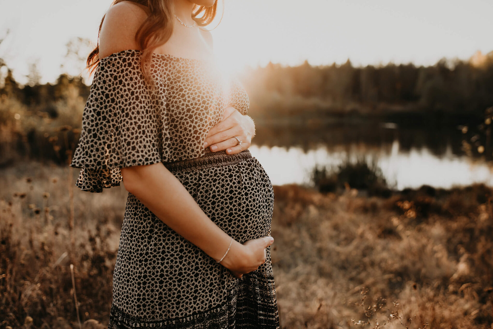 Pregnant woman during photoshoot in Redmond, WA, standing in a field during sunset with pond in the background