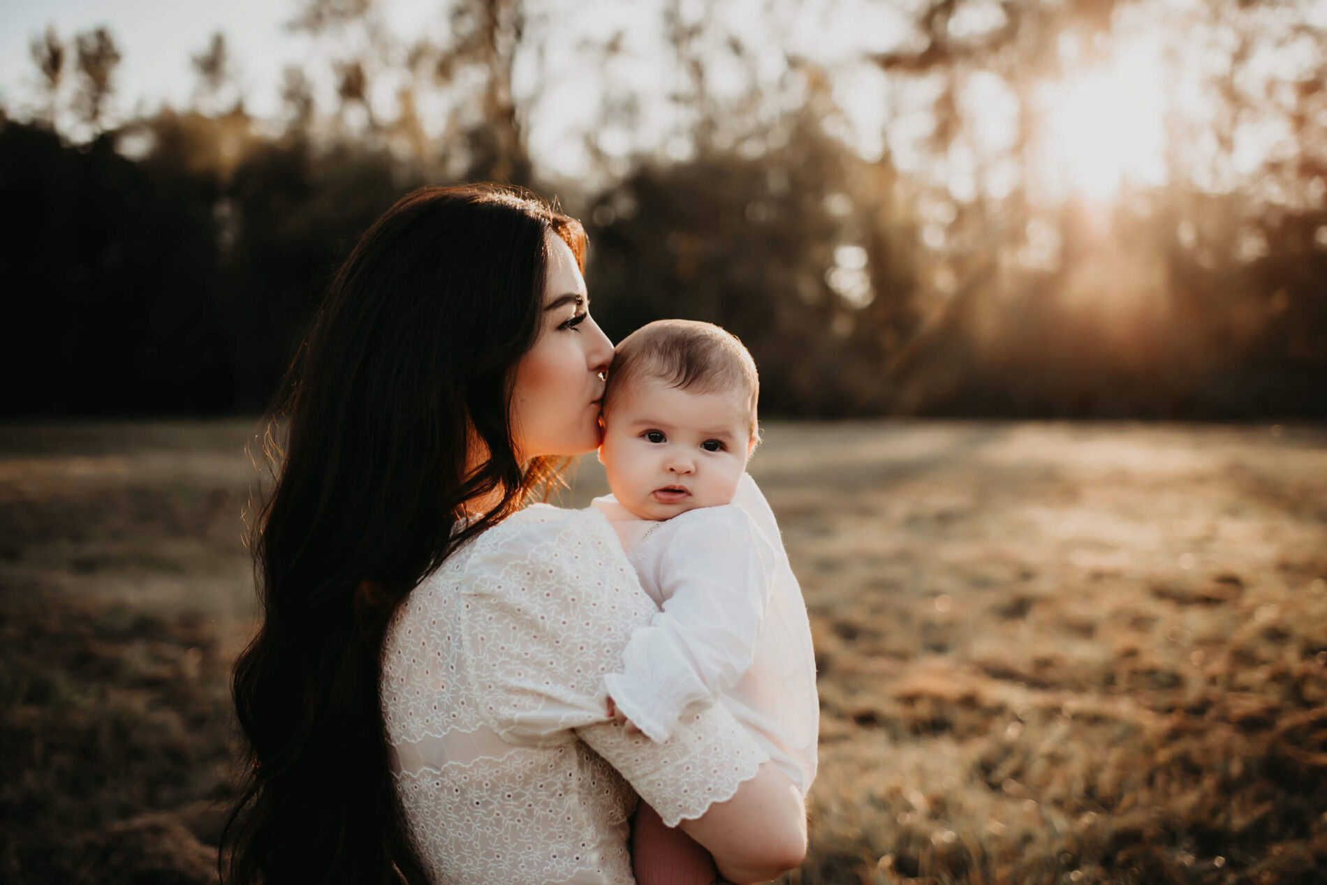 Mom lovingly holding her toddler daughter and kissing her on the side of the head