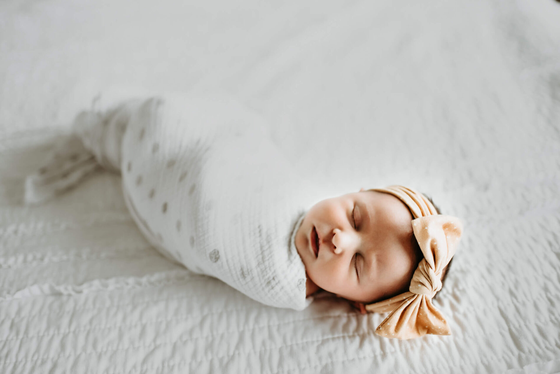 Wrapped sleeping newborn girl on white bed sheets