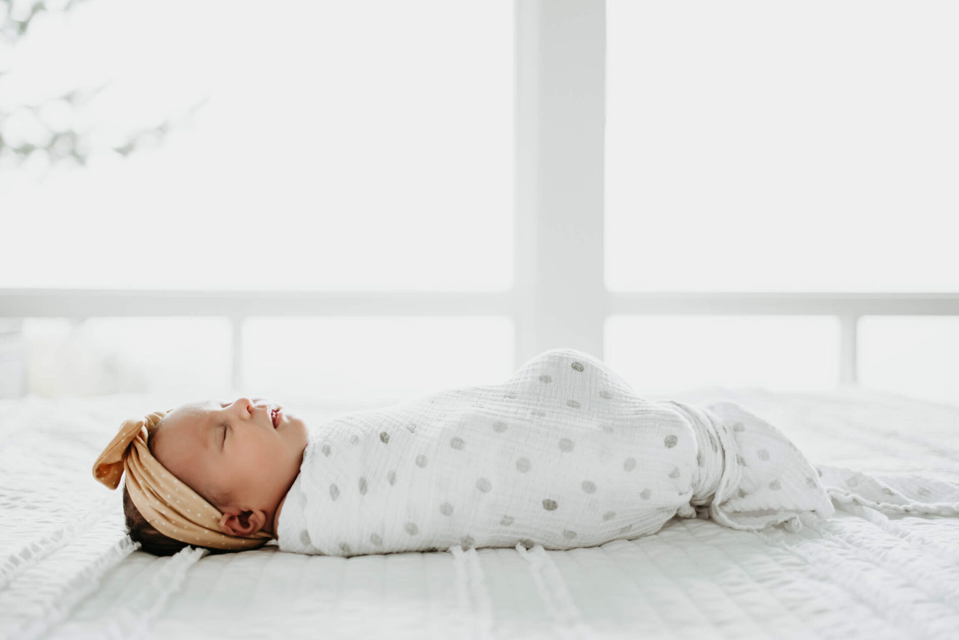 Seattle newborn photo of sleeping wrapped infant lying on a bed with a large window in the background