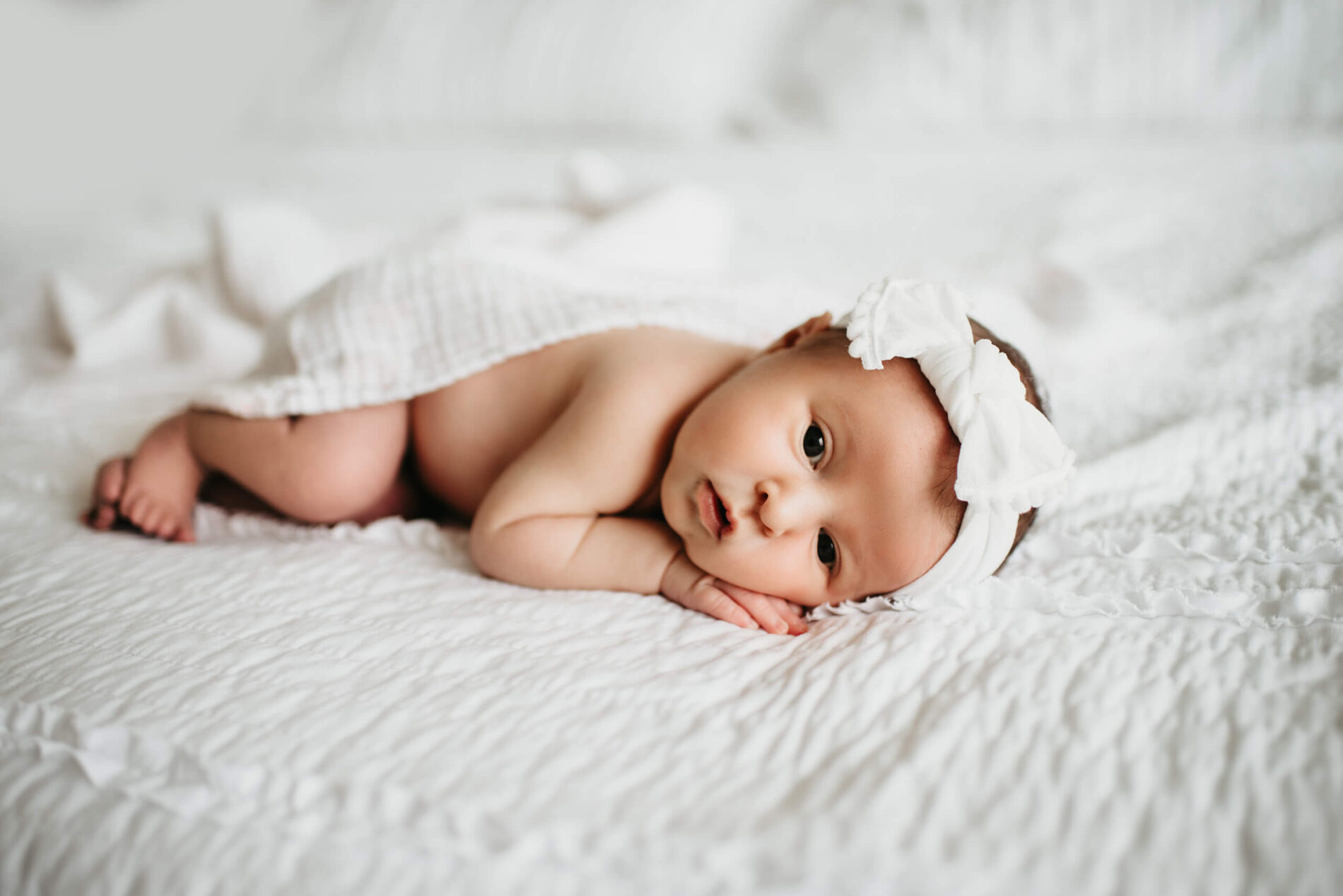 Awake newborn girl lying on top of parent's bed