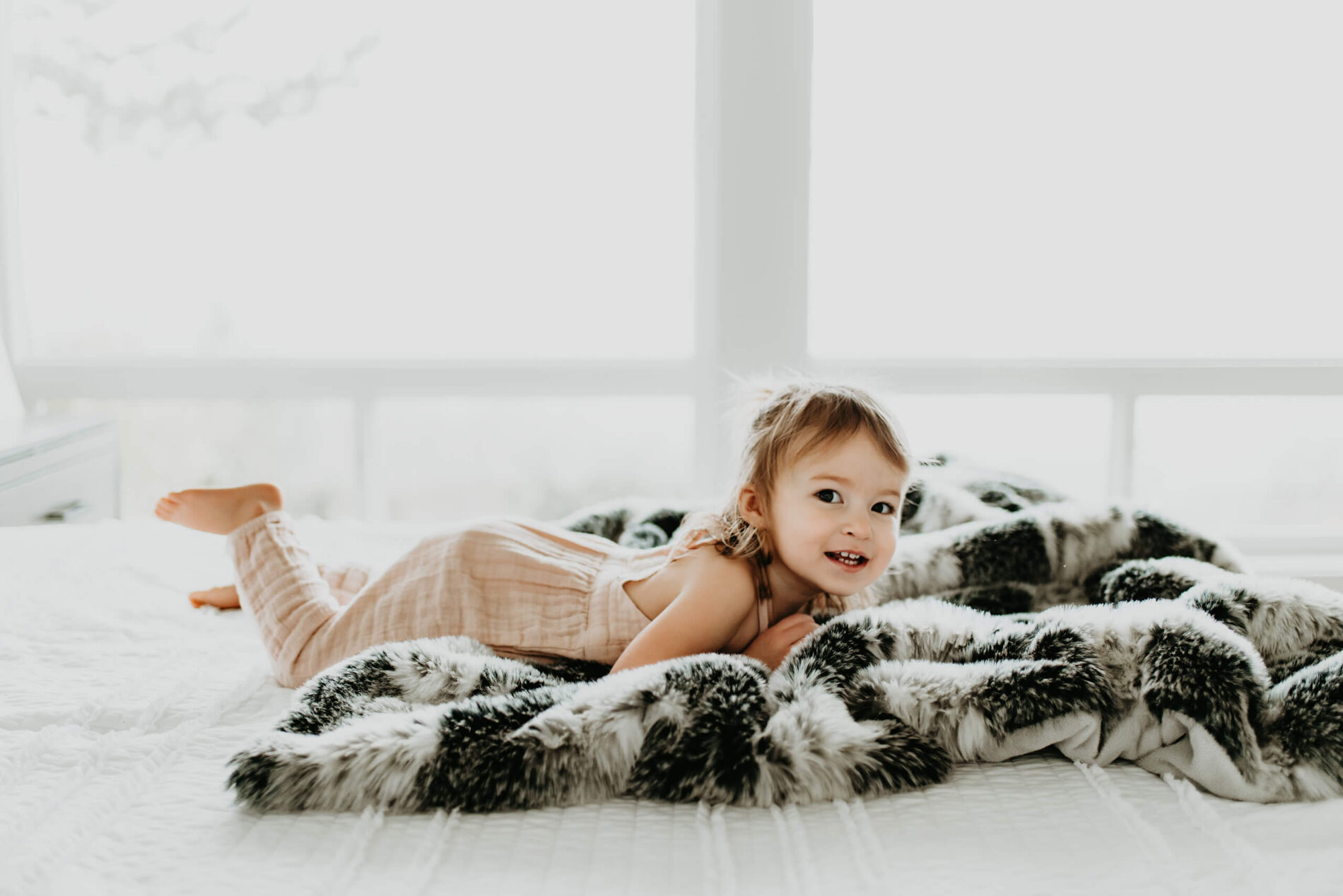 A girl lying on a cozy blanket with large windows in the background