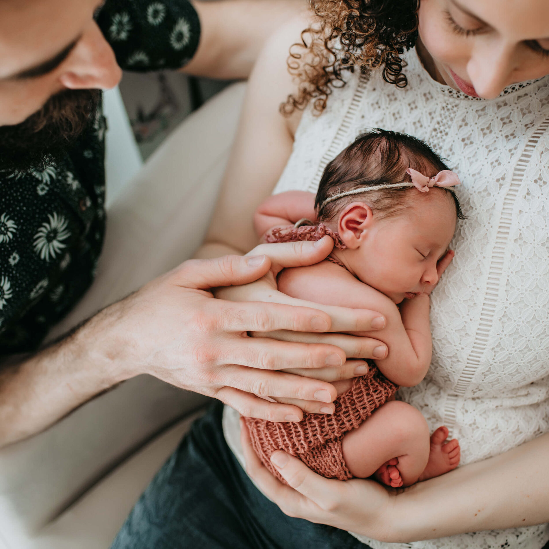 Mom holding her newborn daughter on her chest with dad's hand on the girl's back