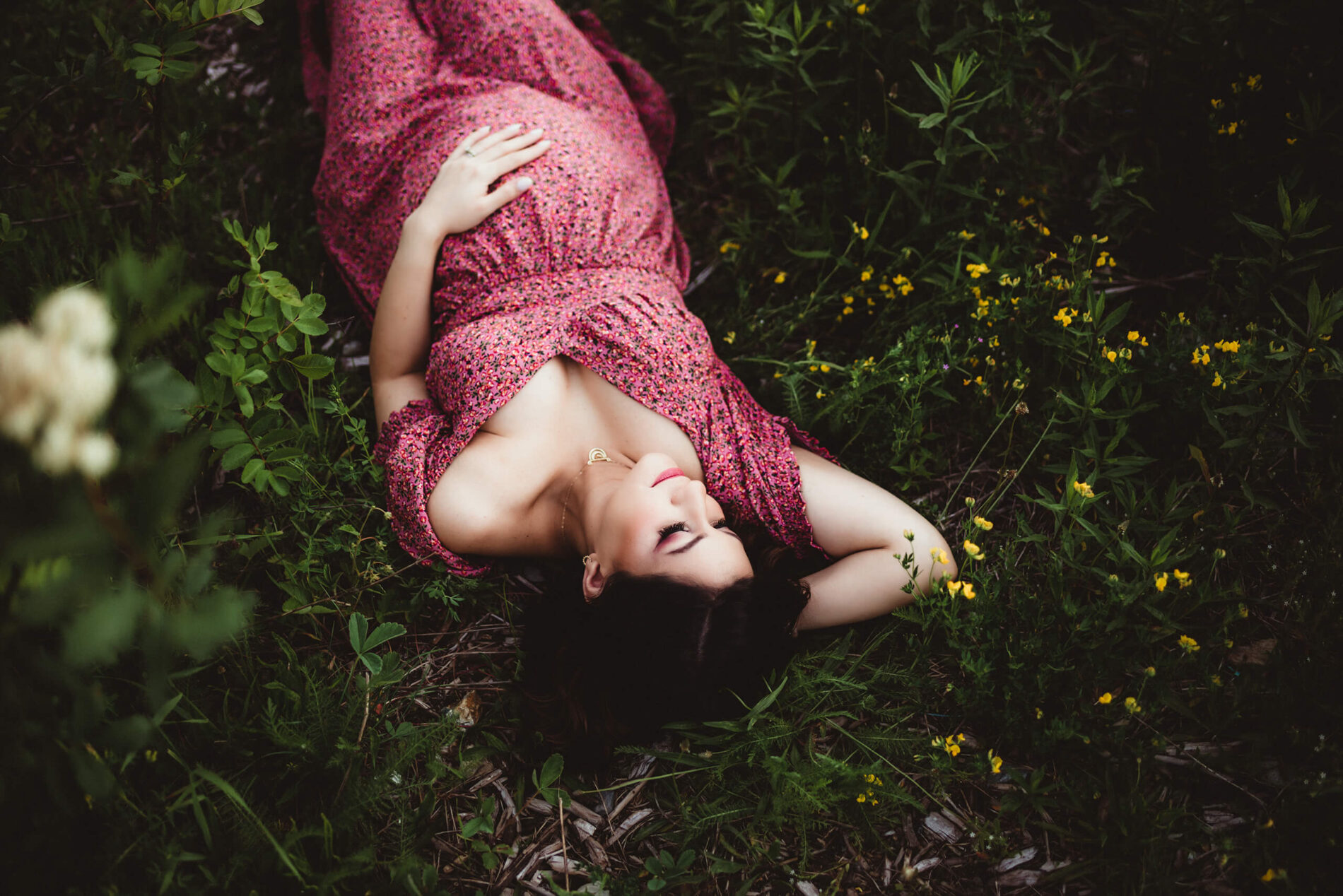 Maternity photoshoot, pregnant woman in a red dress lying in a field of grass and wild flowers at Snoqualmie Pass