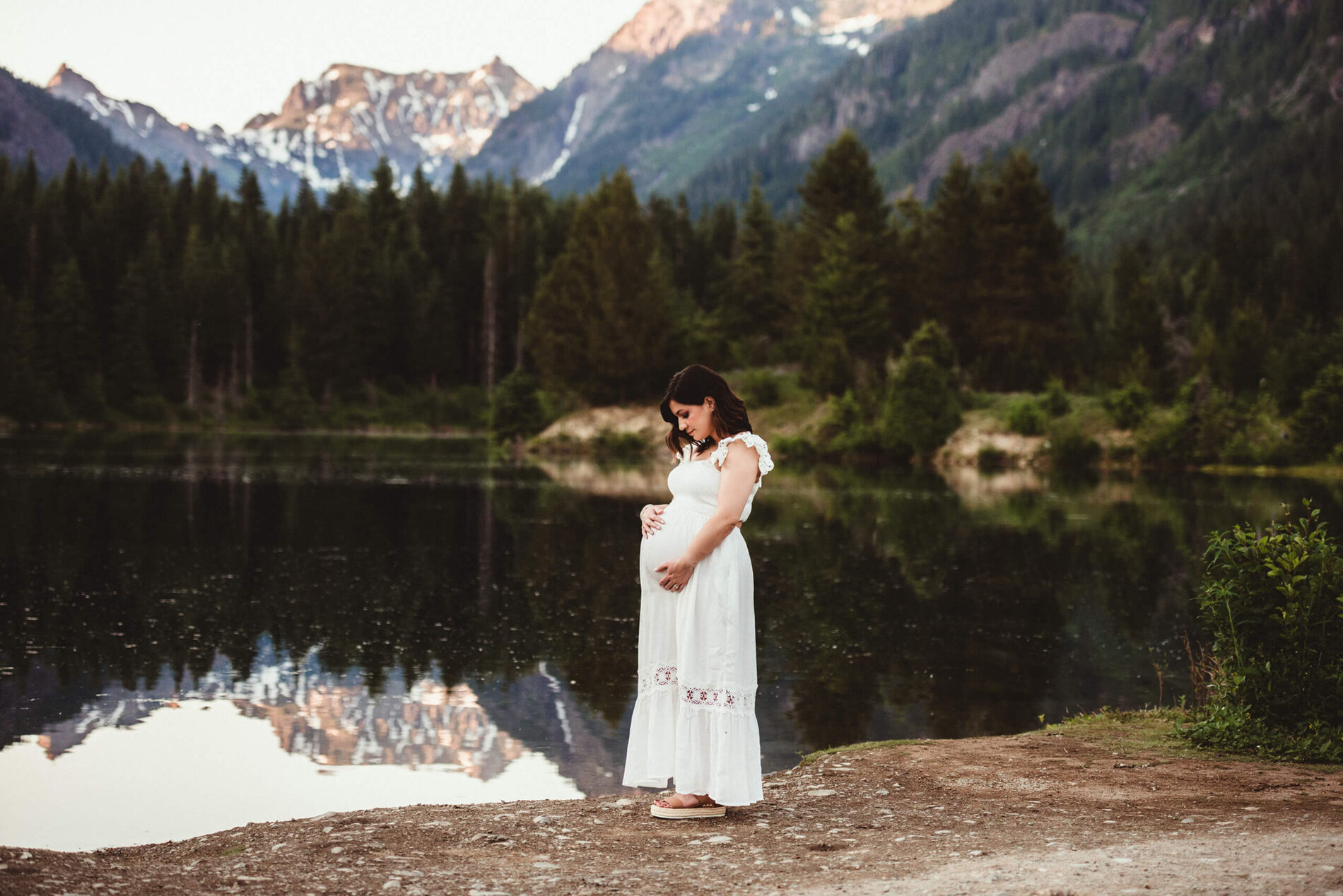 Pregnant woman posing in front of a lake with beautiful mountains in the background