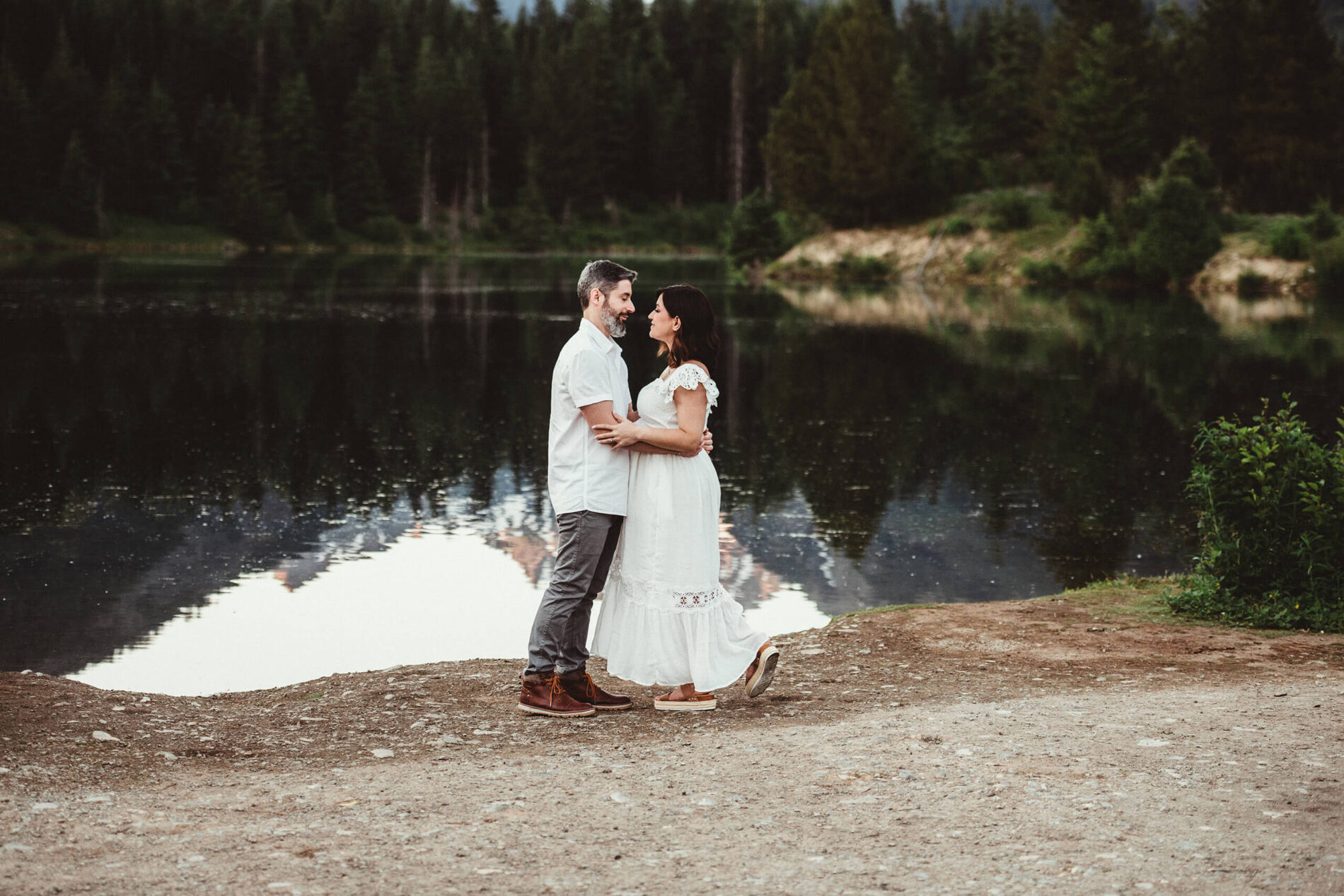 Maternity photoshoot in Seattle, husband and wife facing each other in front of a lake with stunning mountain views