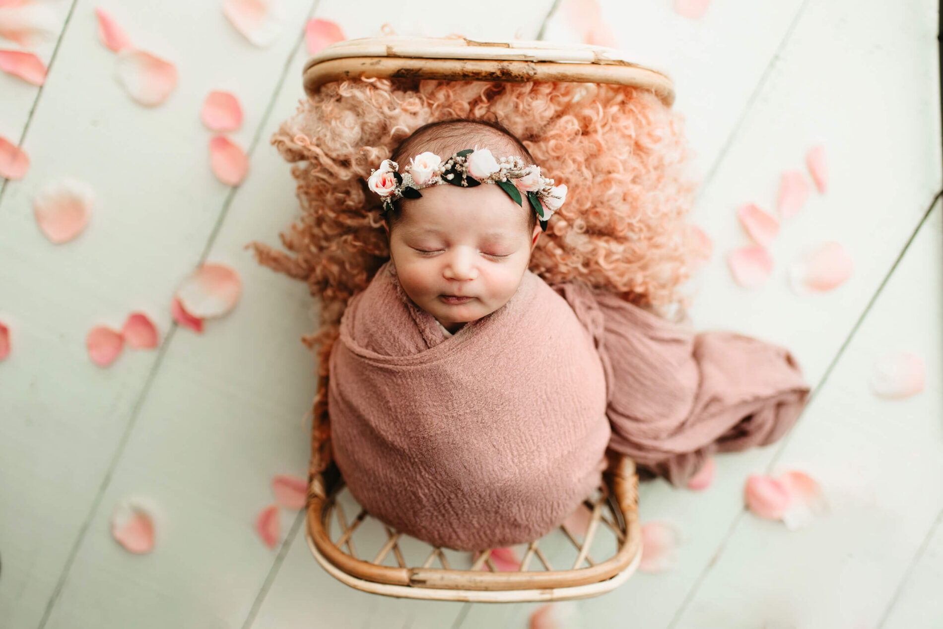 Sleeping newborn girl on a prop bed with flower petals all around