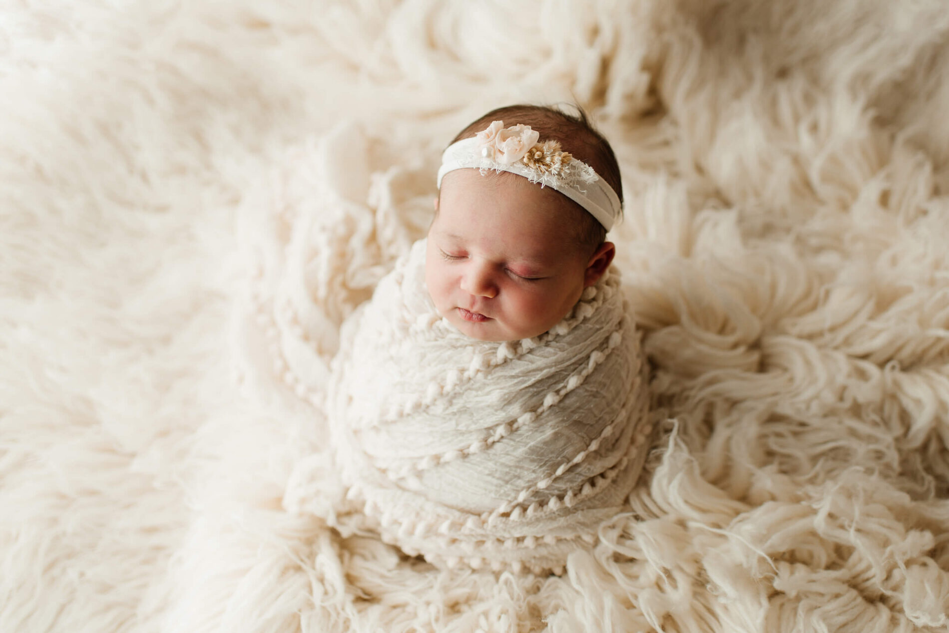 Sleeping newborn girl wrapped in white blanket and wearing a white headband
