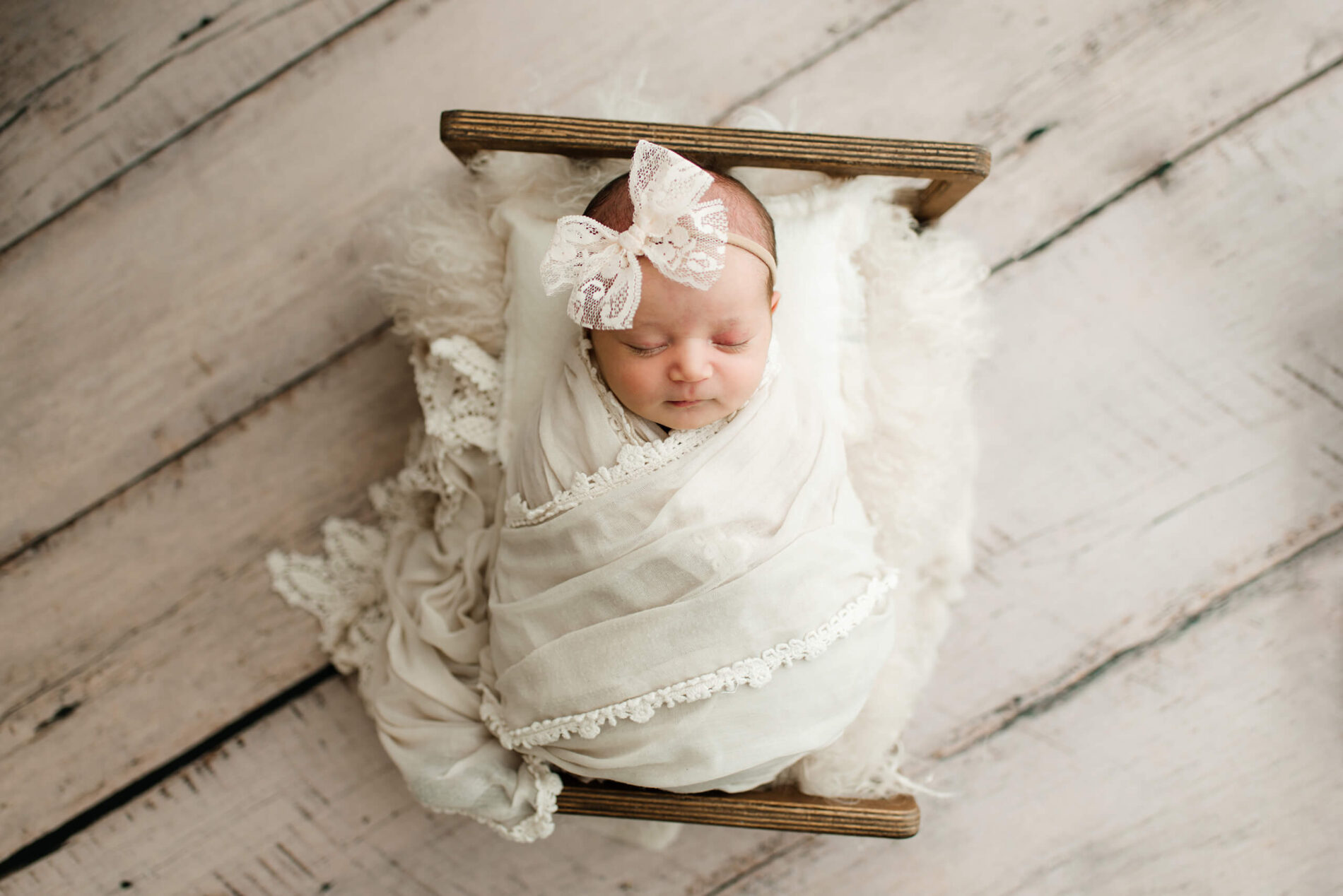 A sleeping newborn girl wrapped in white blankets on a prop bed
