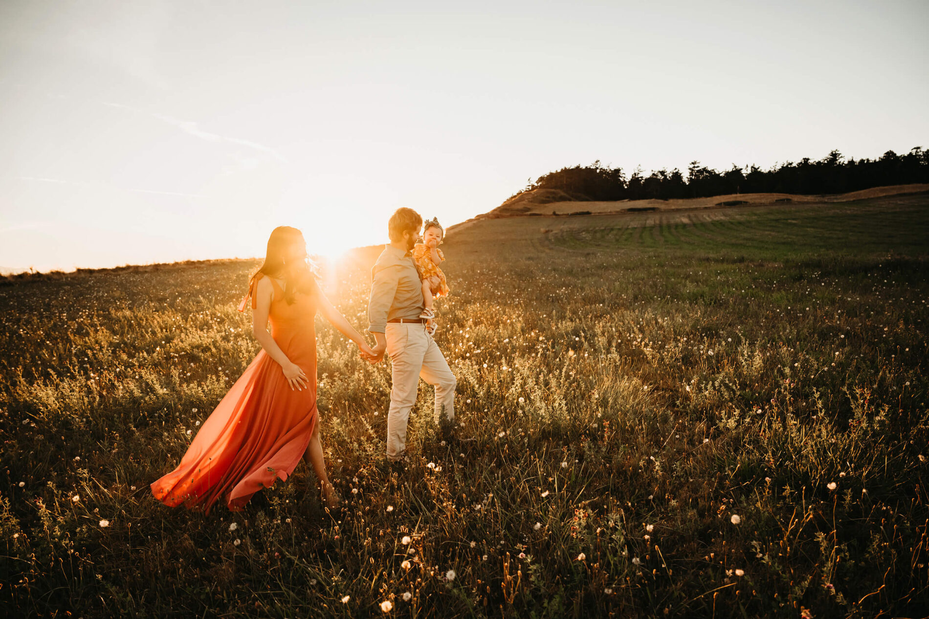 Mom and dad walking with their toddler girl in a meadow at Whidbey Island, WA