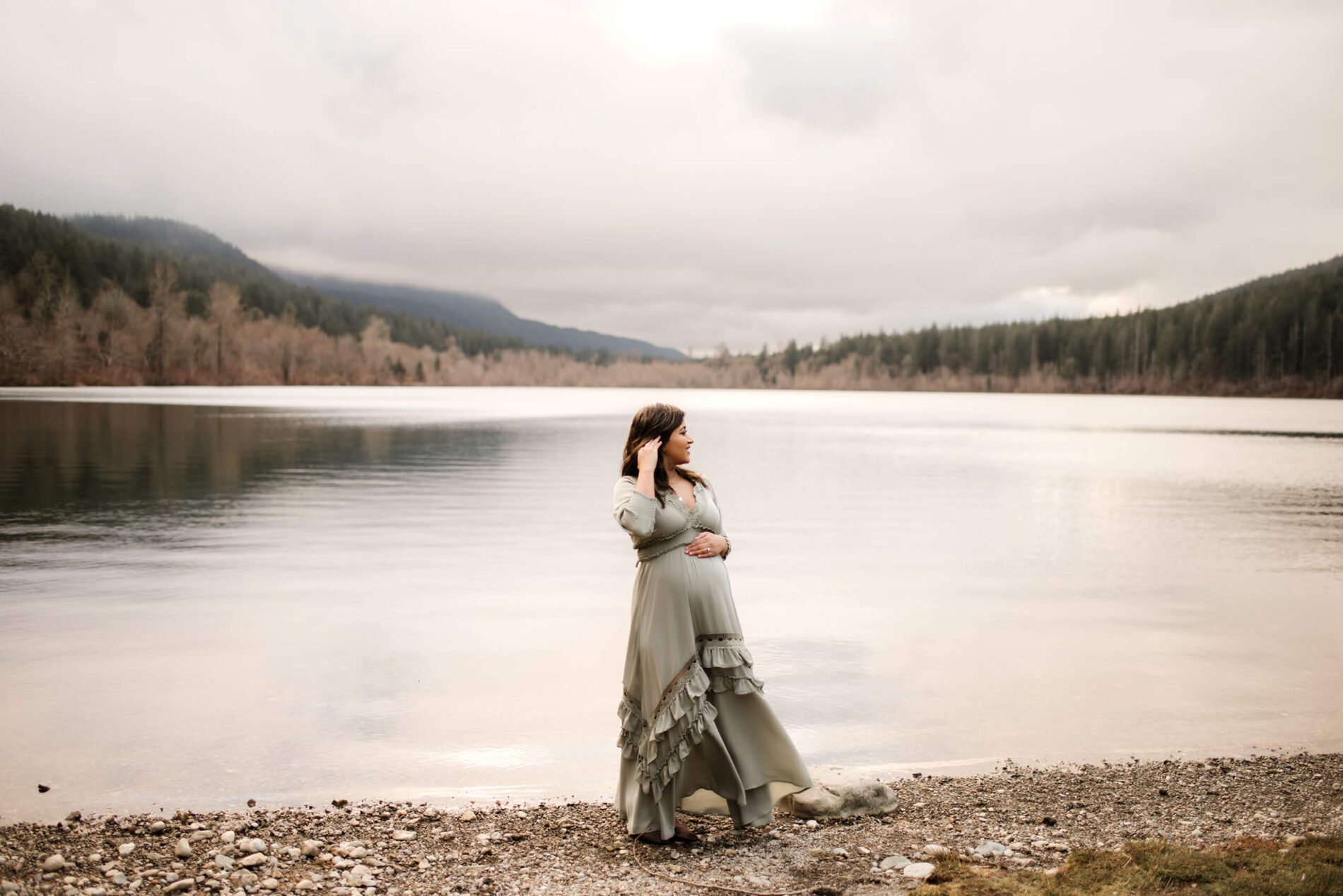 A pregnant woman in a beautiful dress looking into the lake during a winter maternity photo shoot