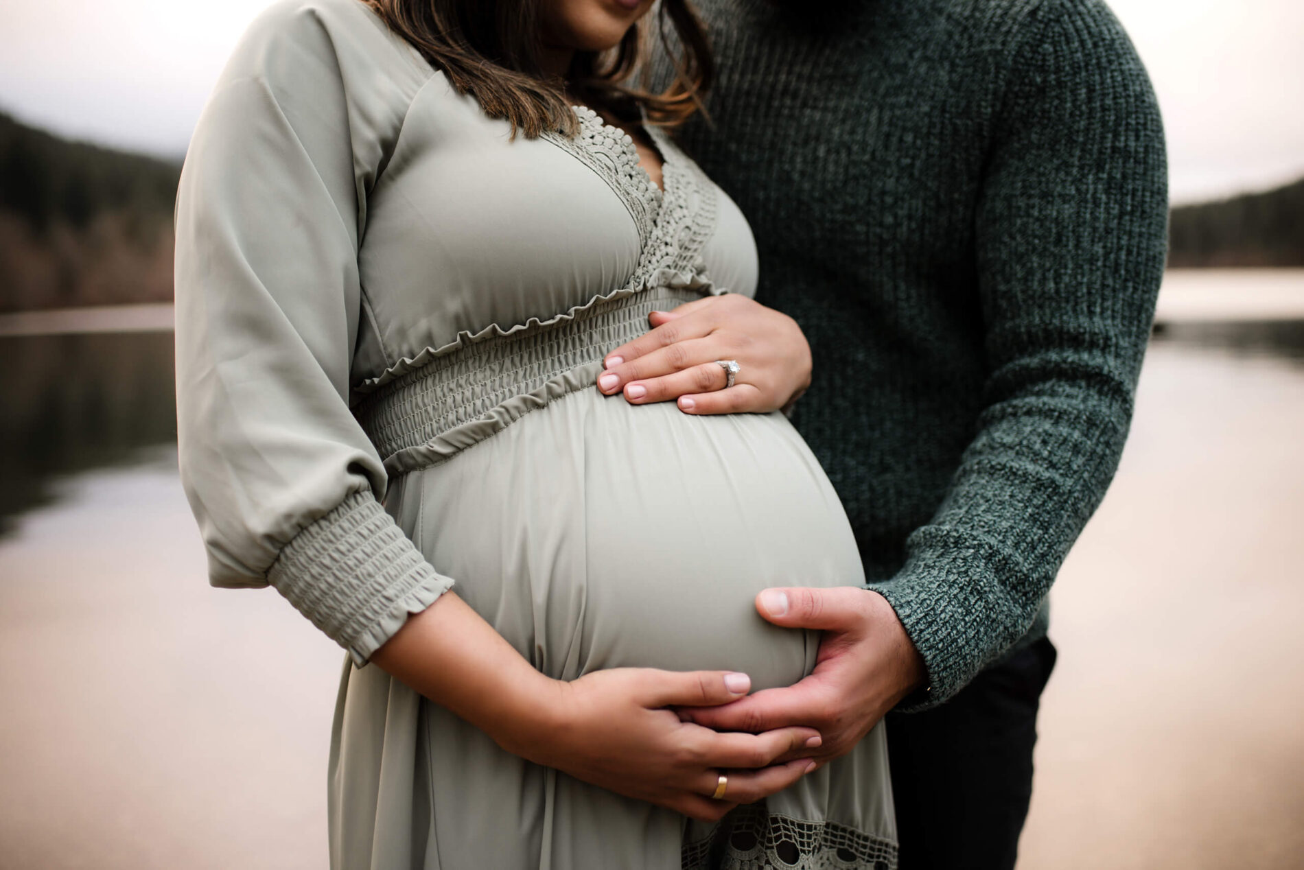 Husband hugging his pregnant wife with his hand on her belly during a winter maternity photo shoot