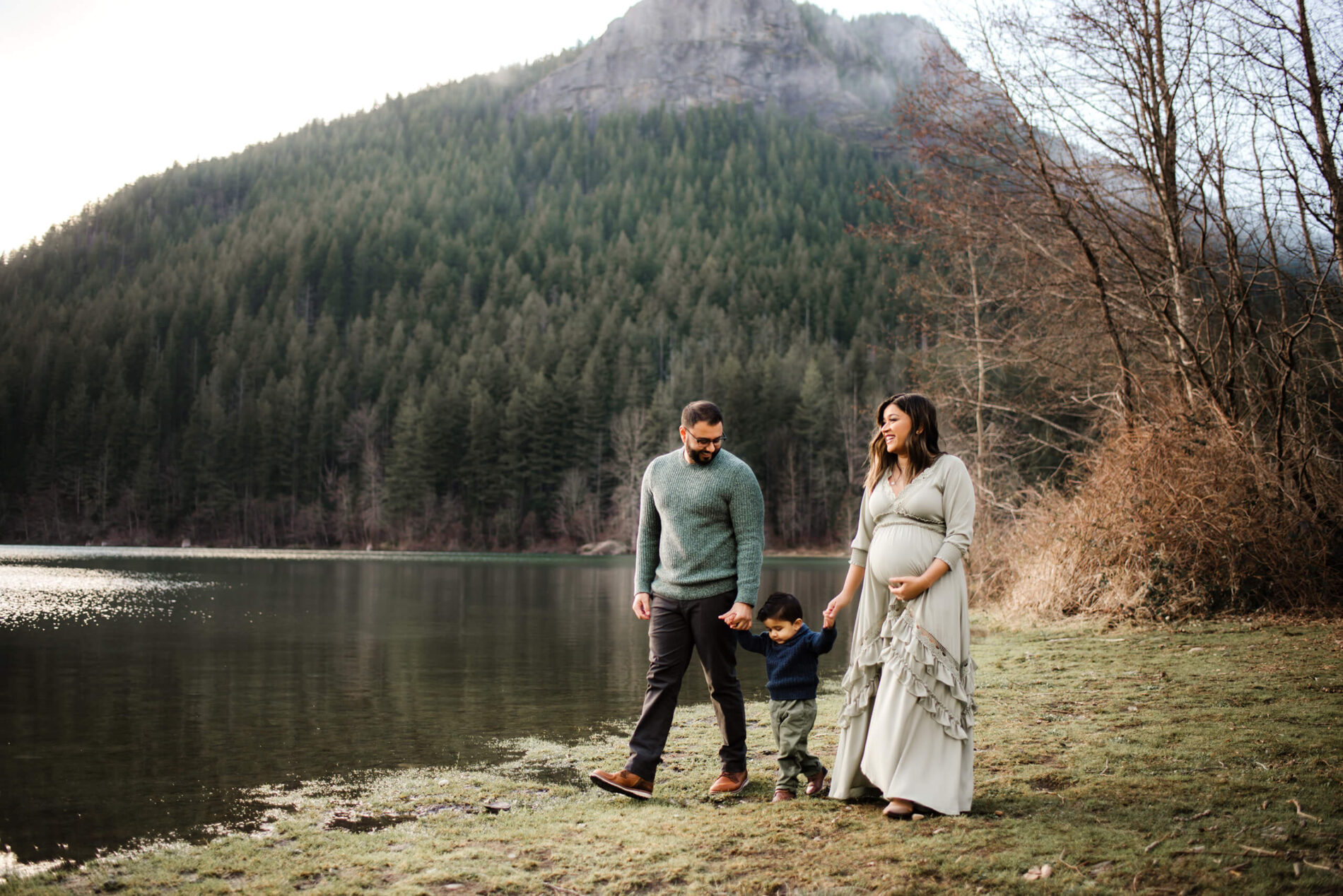 Pregnant woman, walking on a beach with husband and toddler son, with stunning mountain in the background during a winter maternity photo shoot