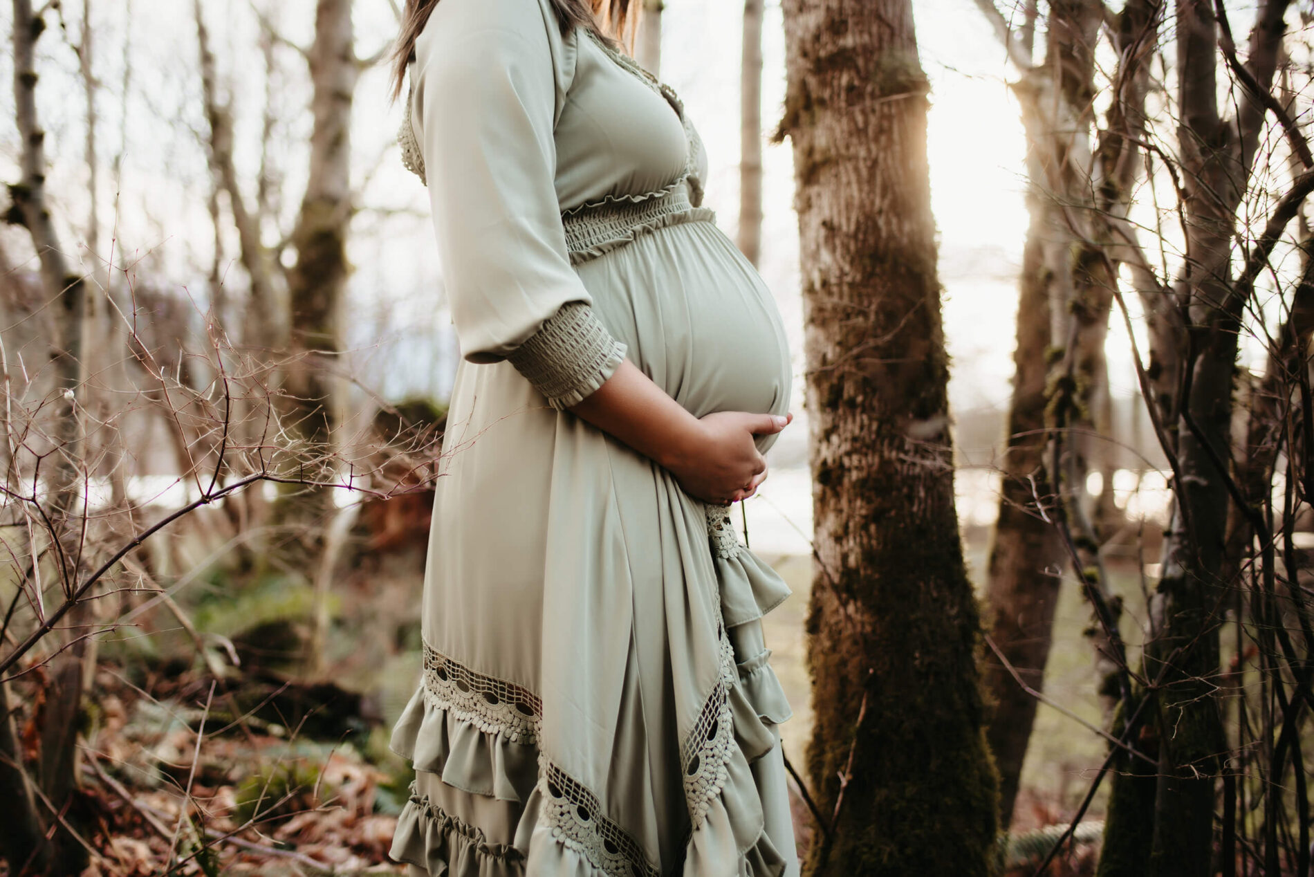 Pregnant woman standing in the woods during sunset winter maternity photo shoot