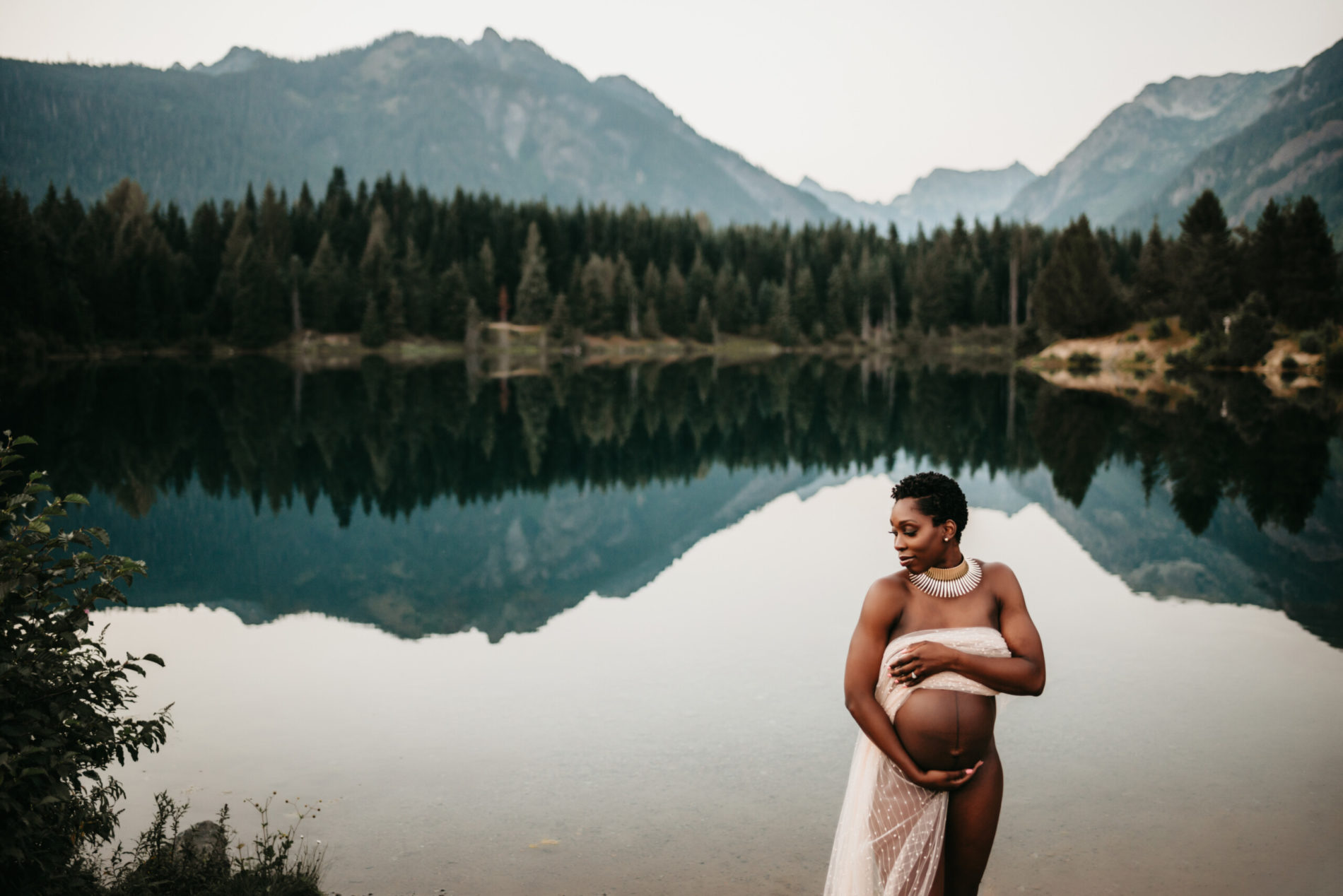 A beautiful pregnant woman posing during maternity photo shoot in front of a stunning lake with mountains in the background