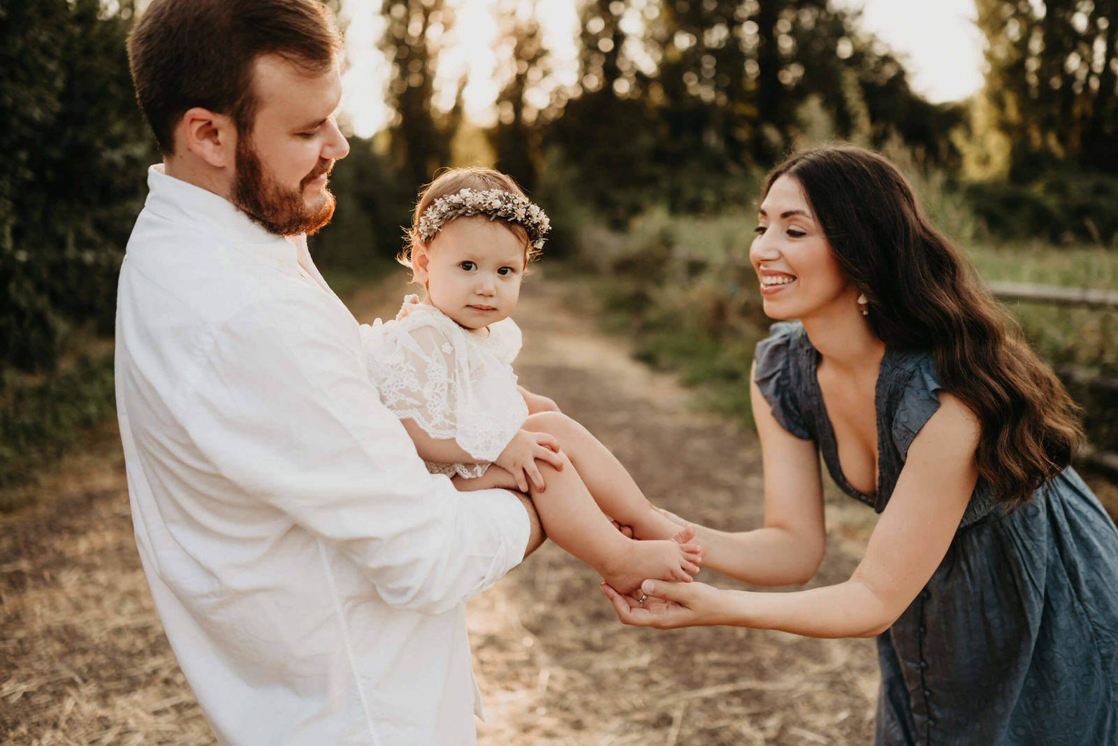 Mom, dad, and their young daughter playing together in a field at sunset.