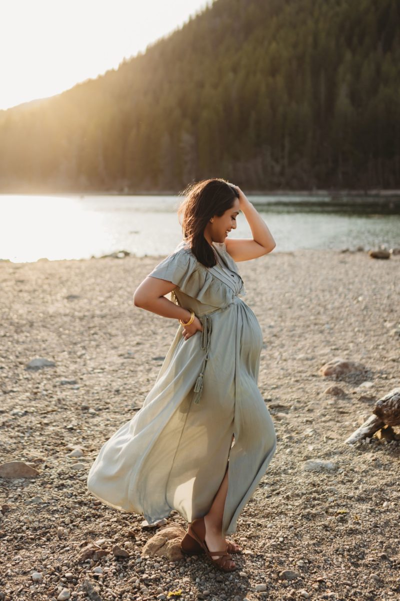 A pregnant woman in a maternity gown posing in front of a lake
