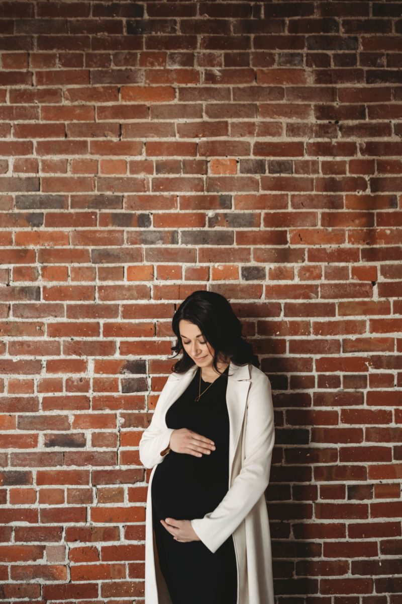 A pregnant woman standing in front of wall of red bricks