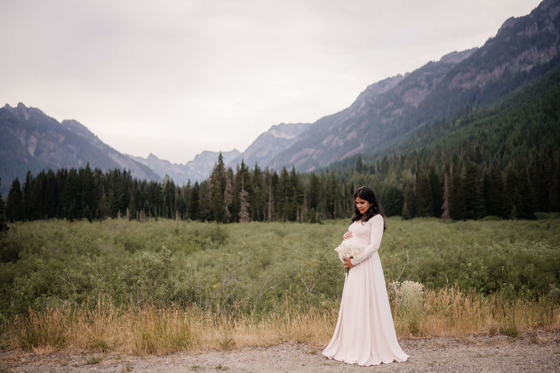 Pregnant woman holding flowers by her belly with beautiful mountains in the background