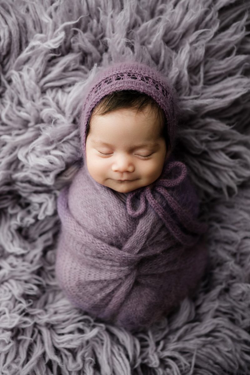 A beautiful newborn girl, masterfully wrapped, smiling in her sleep