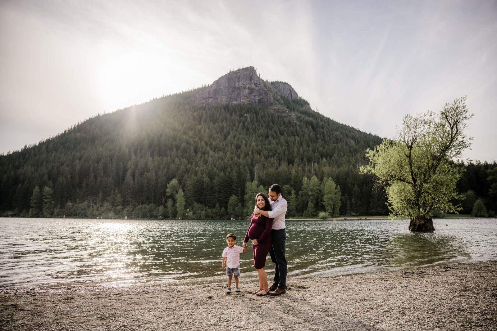 Pregnant woman with her husband and toddler son by a beautiful lake with mountains in the background
