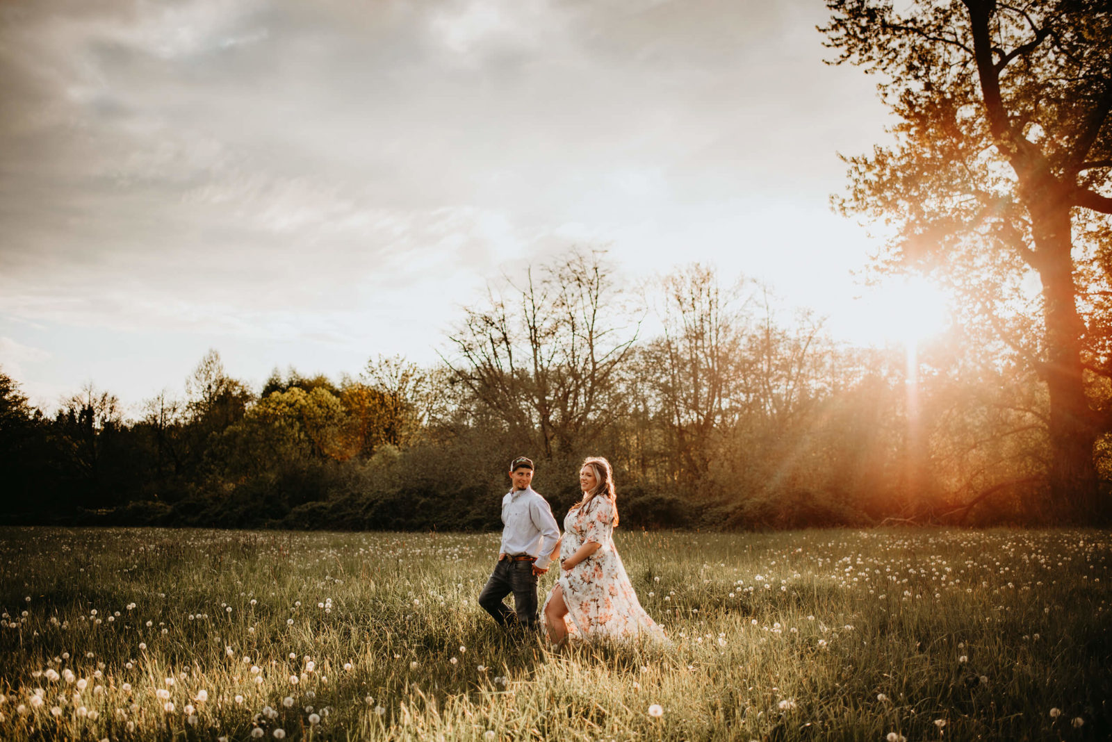 Pregnant woman in a beautiful dress walking with her husband in a sunlit meadow