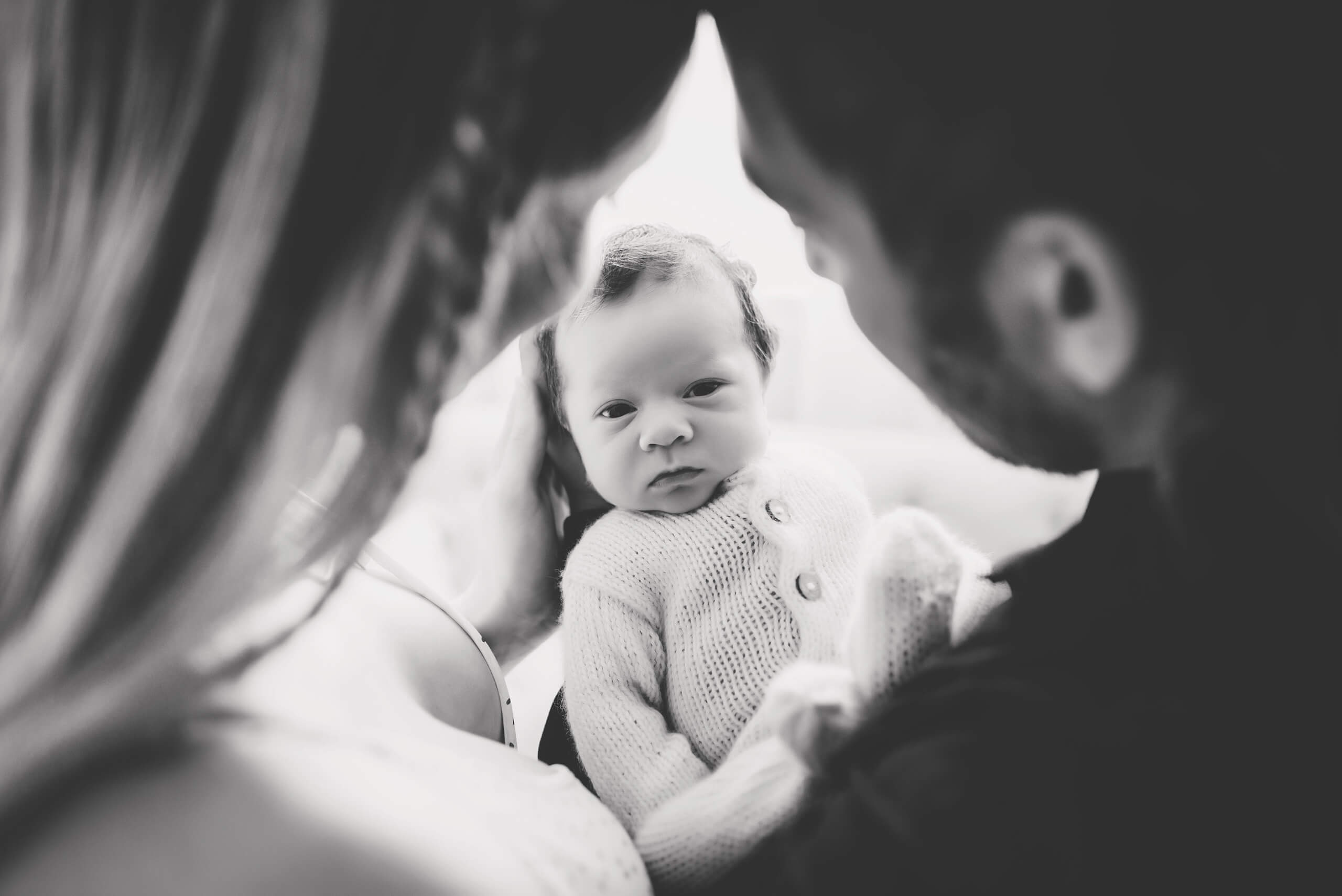 Baby looking at the camera while being held between parents in a black-and-white family portrait