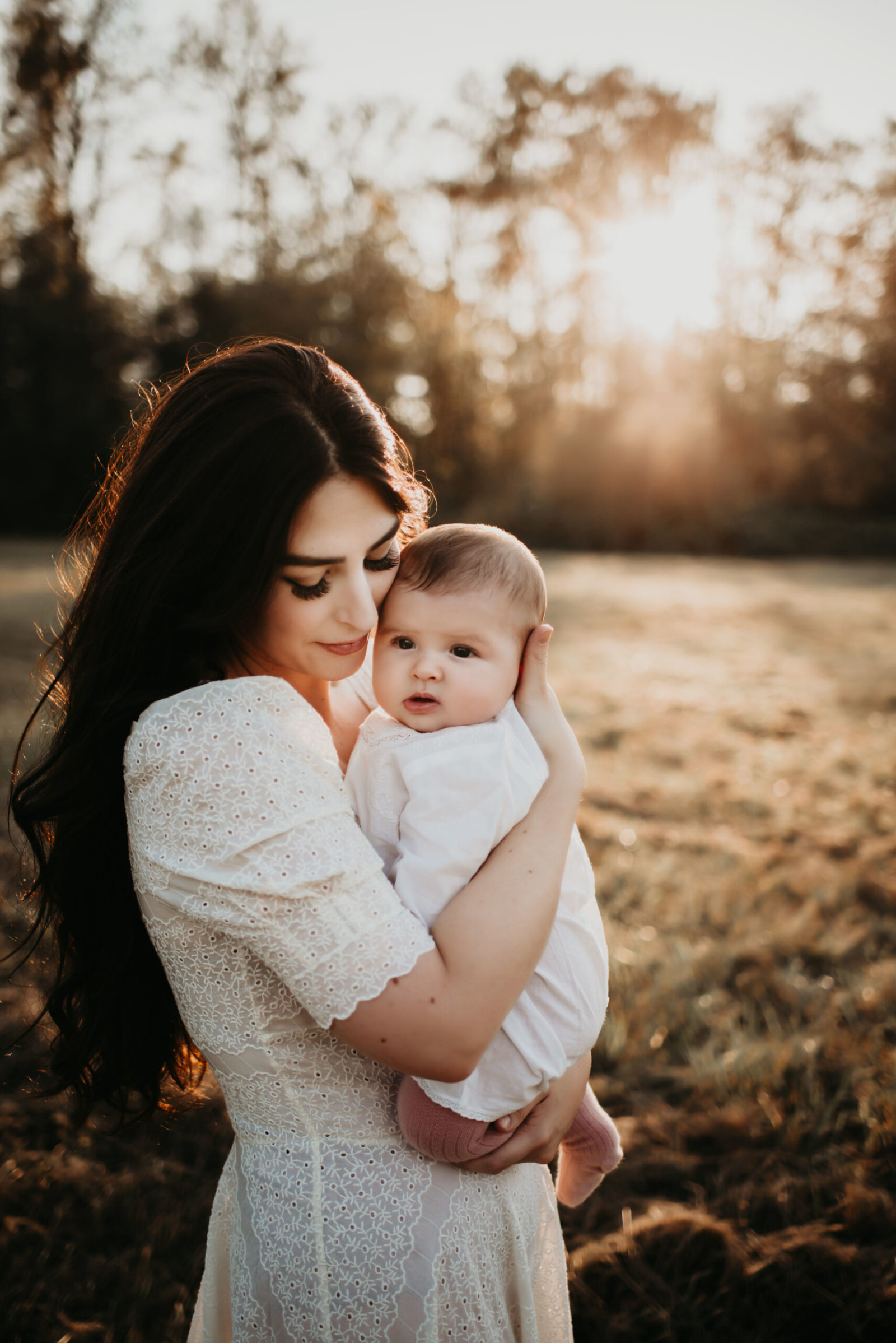 Summer Seattle family photoshoot: mother in a white dress holding her daughter in her arms during beautiful sunset