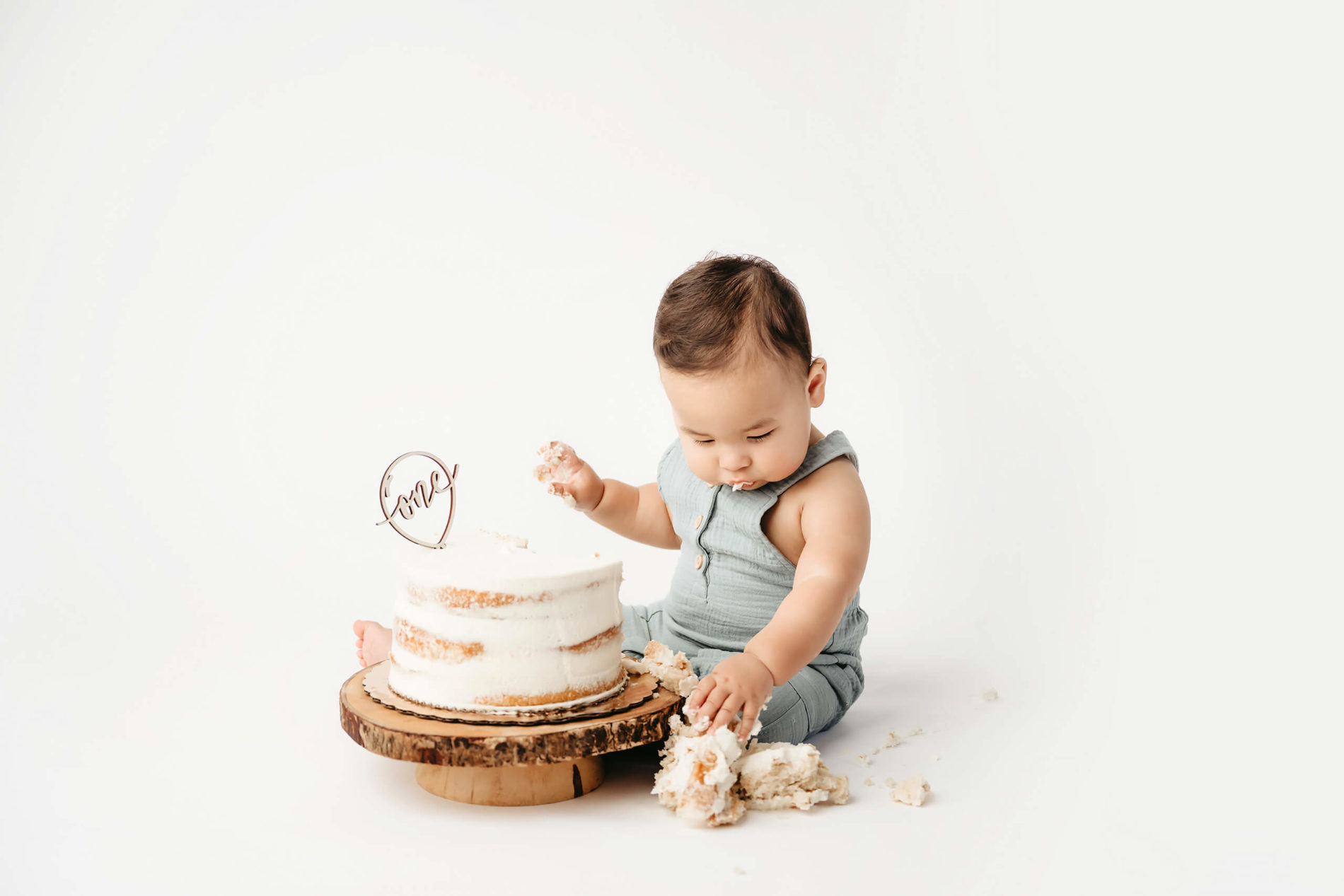 Adorable one-year-old boy exploring a cake on the floor of a photography studio