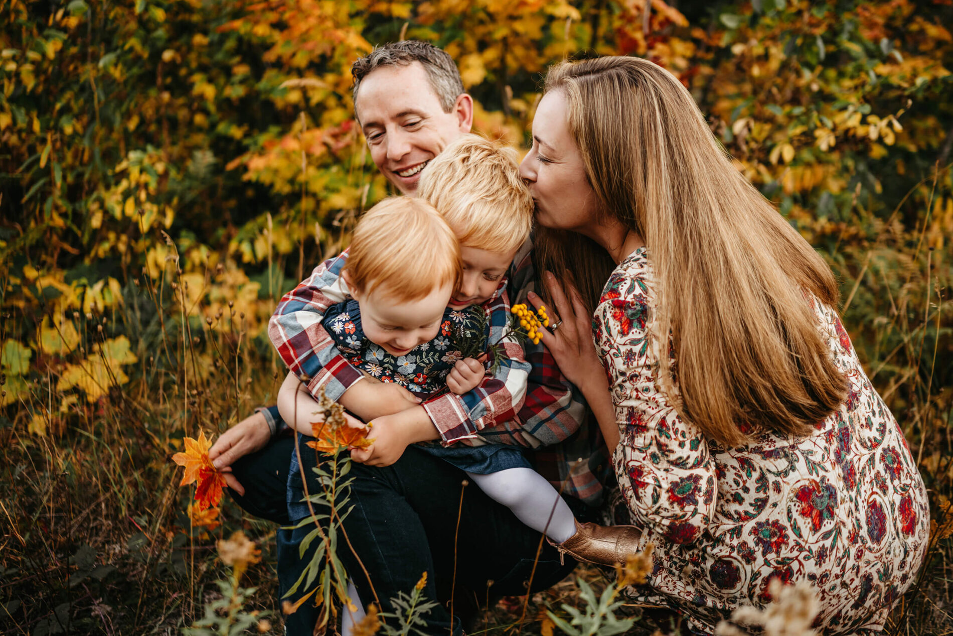Seattle family photo shoot, mom, dad, and two kids hugging in a wildflower field with fall foliage all around
