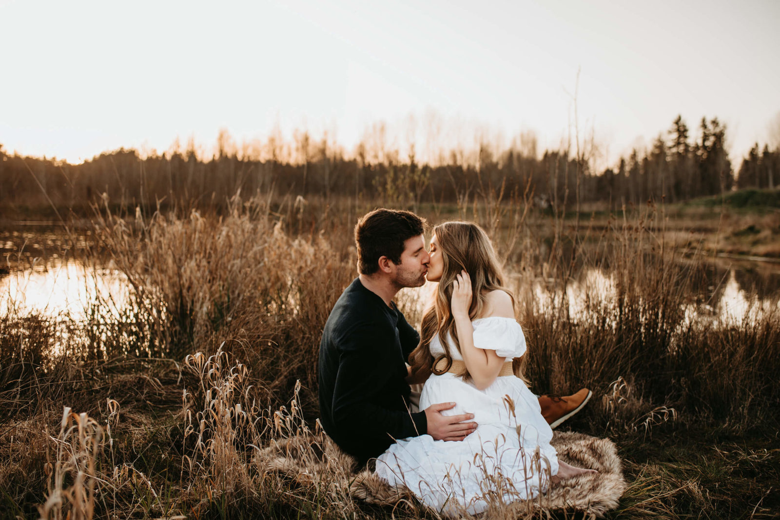 Pregnant woman kissing her husband while he is lays a hand on her stomach