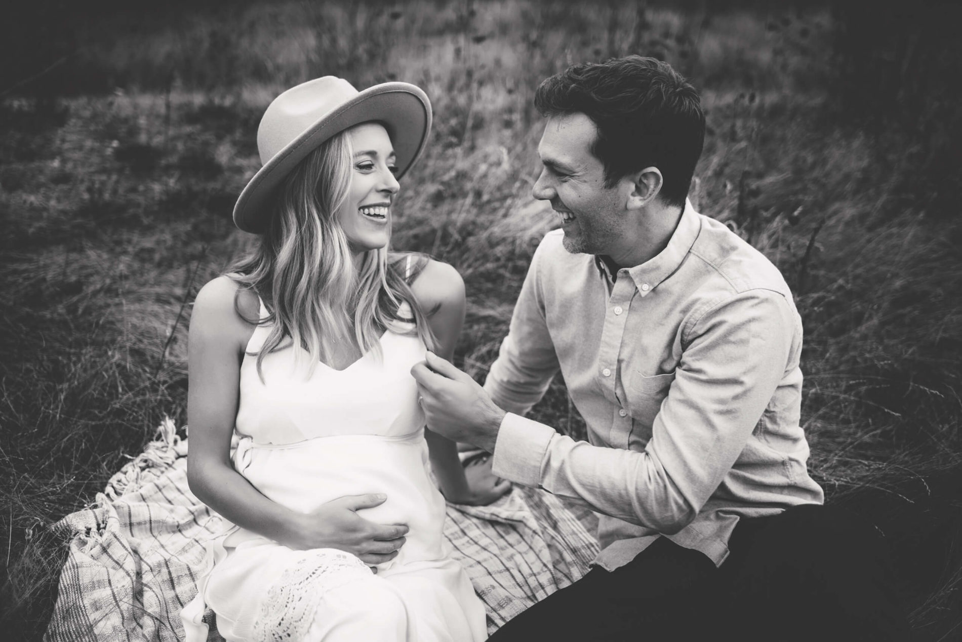 Black and white photo of a laughing pregnant woman with her husband in a field
