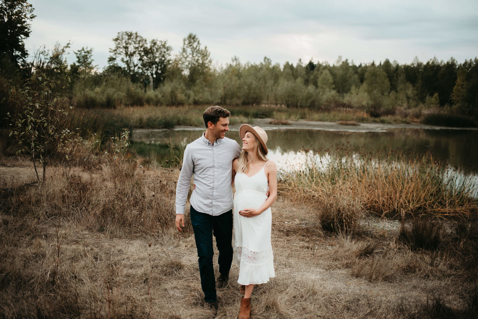 A man hugging lovingly his pregnant wife with a pond in the background