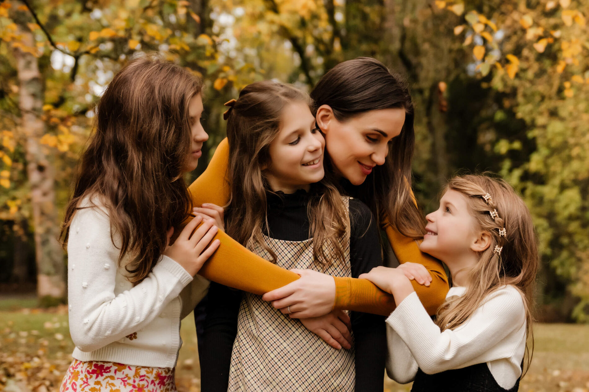 Mom hugging with three daughters with fall foliage in the background