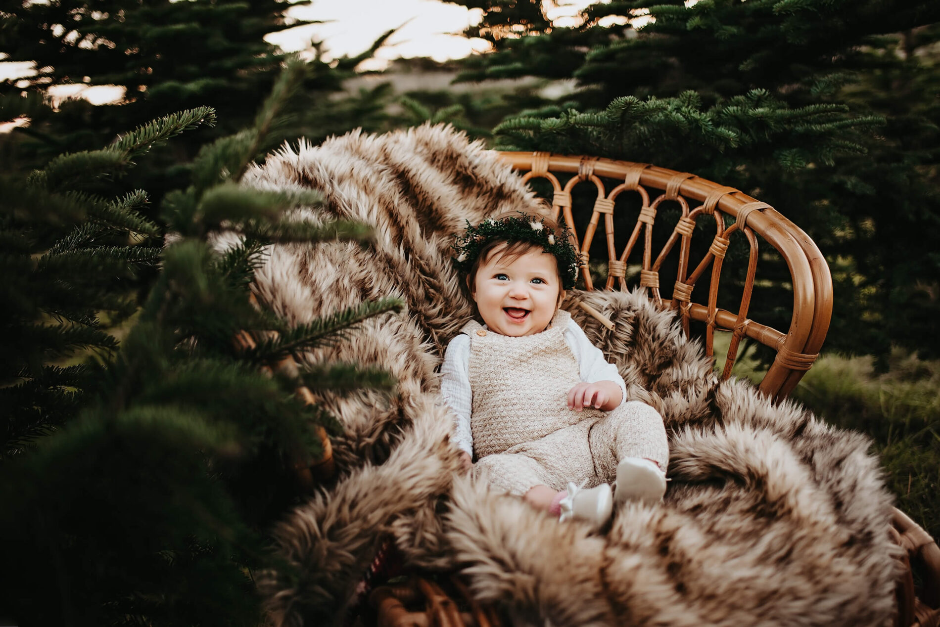 A cute toddler girl sitting on a cozy blanket in a chair at a Christmas tree farm
