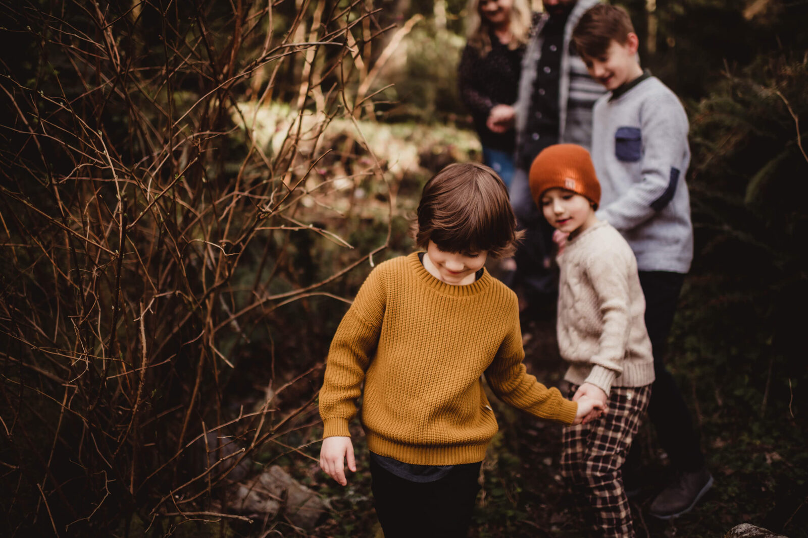 Three brothers walking hand in hand, with parents blurred in the background