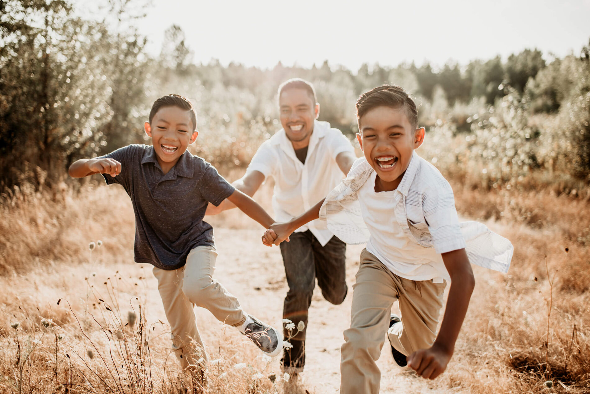 Dad chasing his two sons in a field, everyone is laughing and smiling
