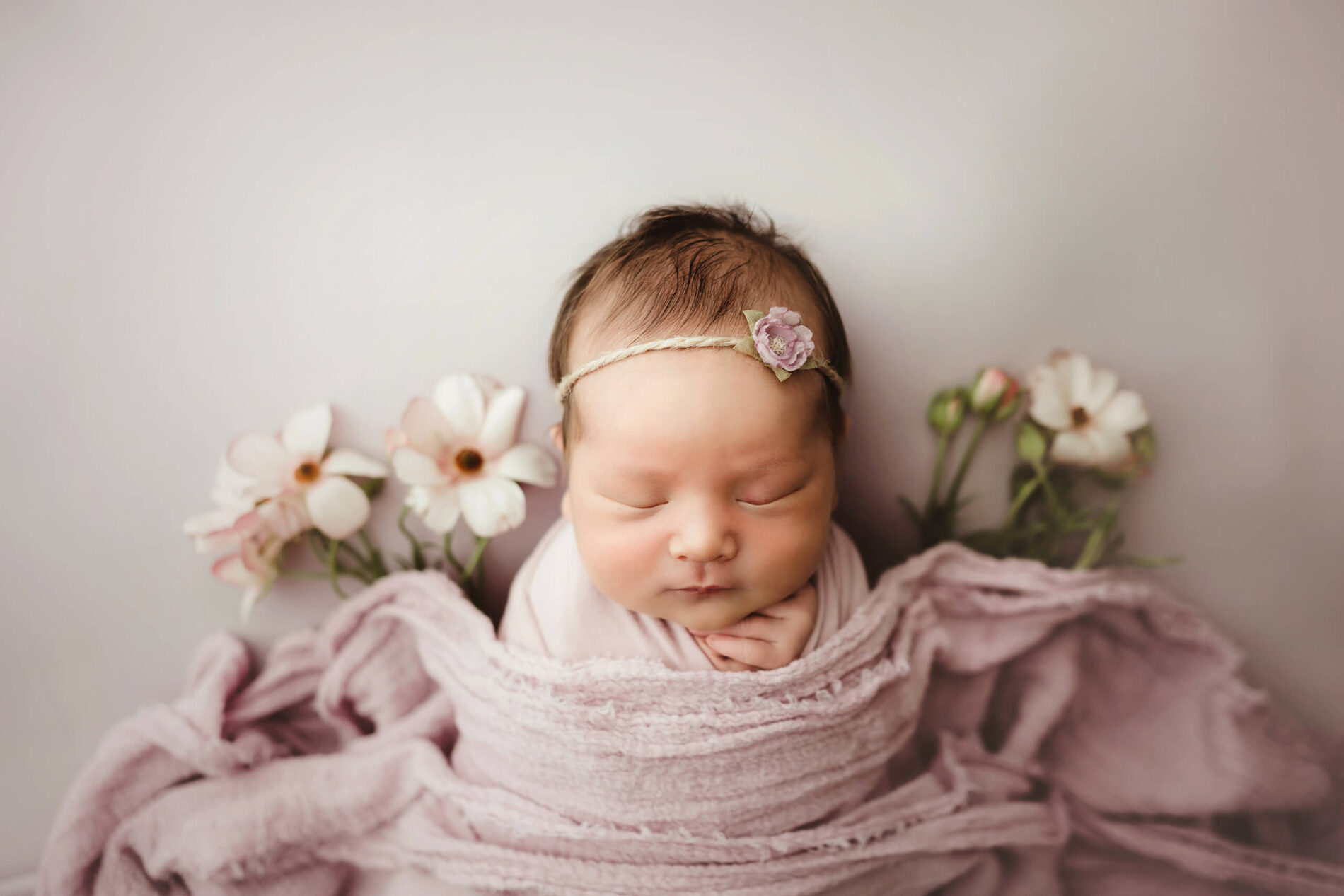 A sleeping newborn girl under wraps with fresh flowers all around her