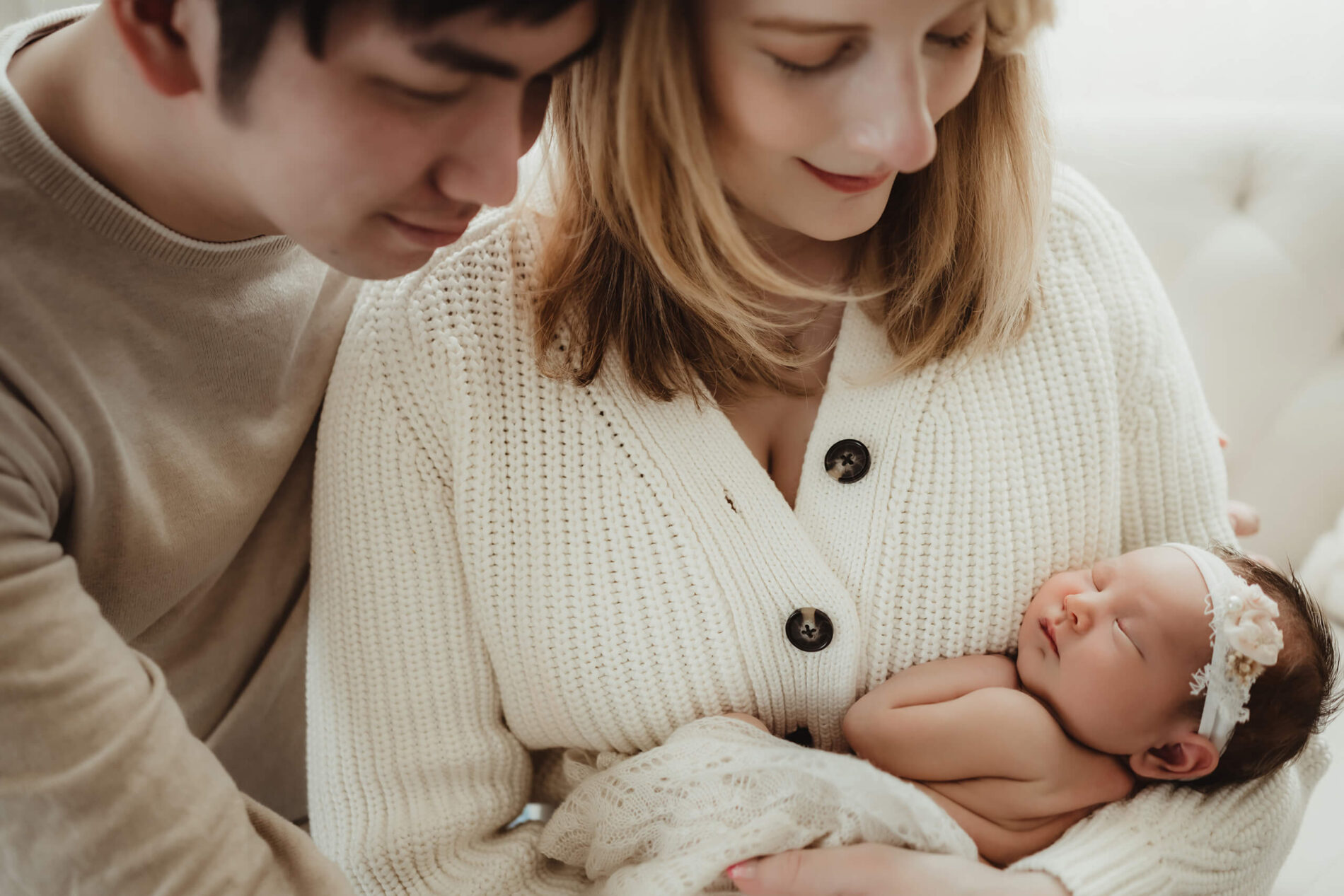 Woman holding her newborn daughter in her arms, hugged by her husband