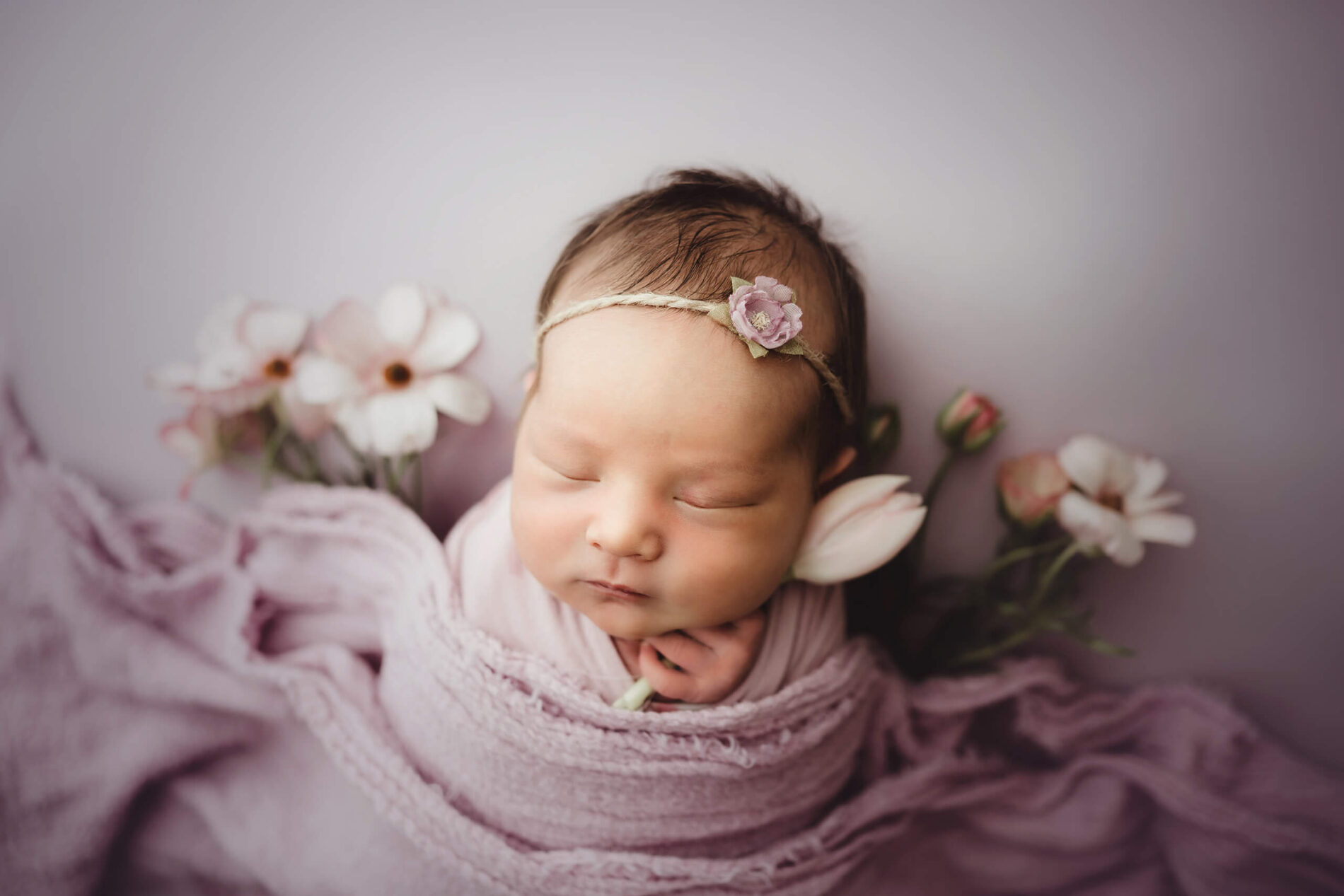 A newborn girl sleeping, masterfully wrapped and surrounded by fresh flowers