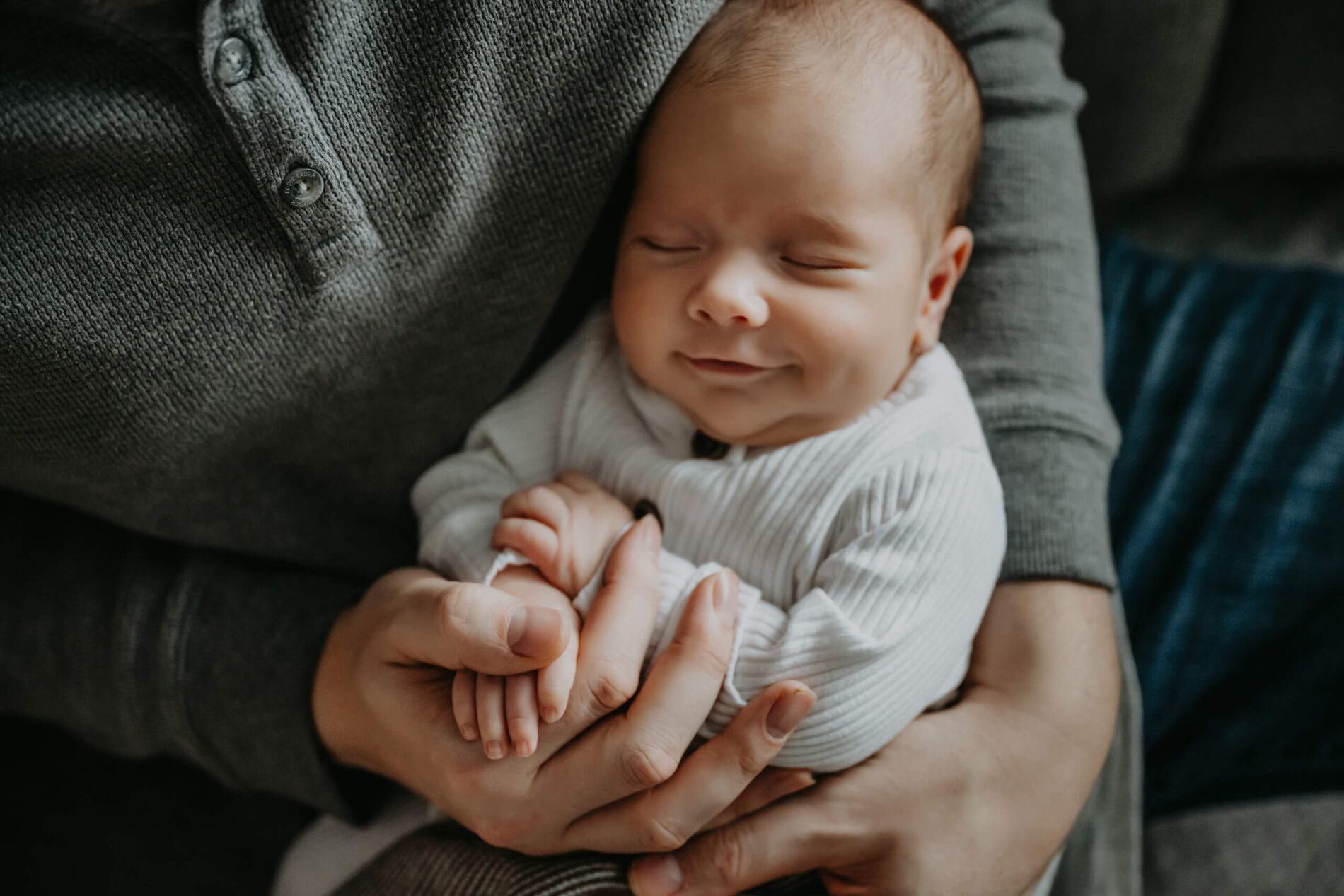 Sleeping newborn boy smiling in his father's arms