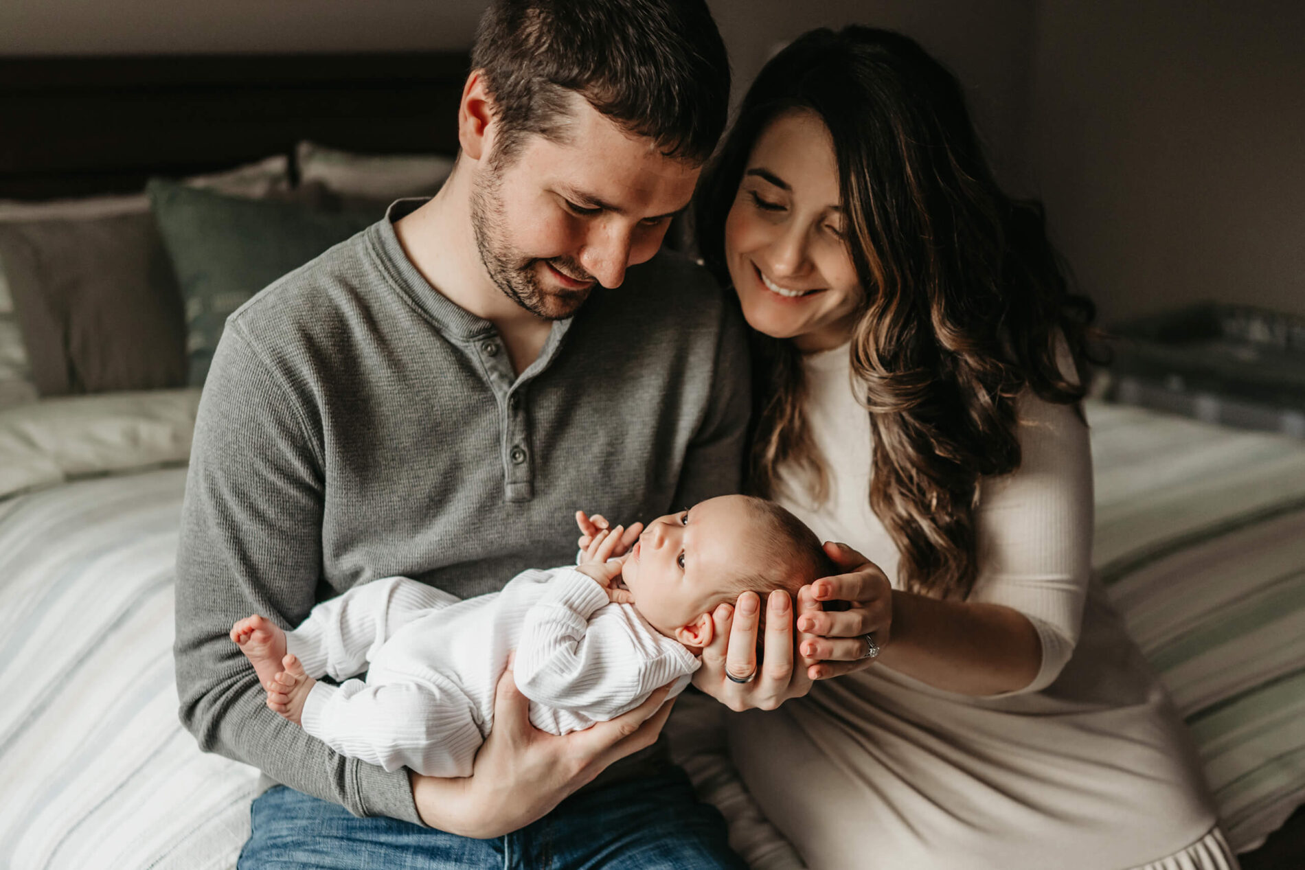 Mom and dad sitting close together on their bed, looking at their newborn son