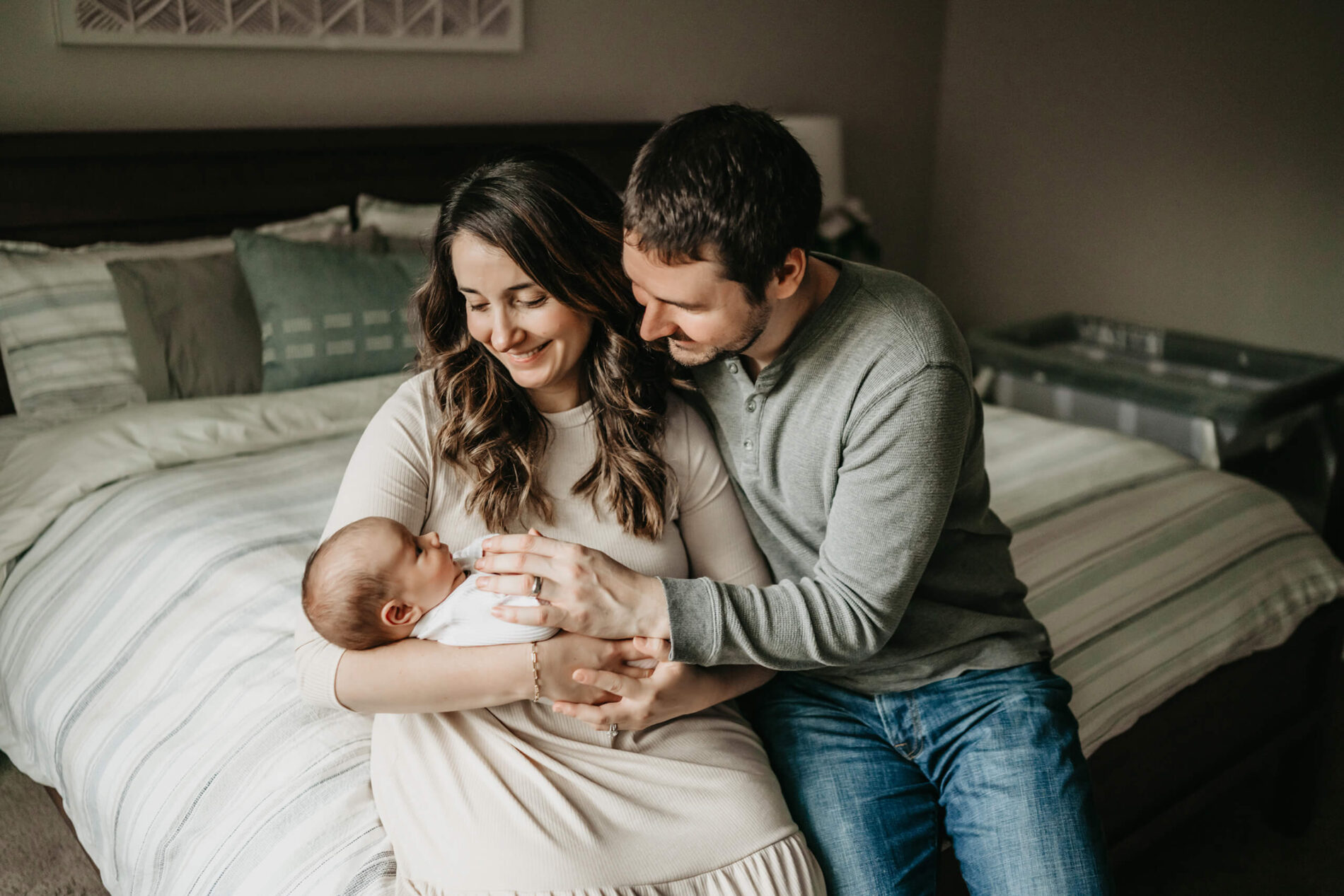 A woman sitting on her bed in her bedroom holding her newborn son, with her husband sitting next to her