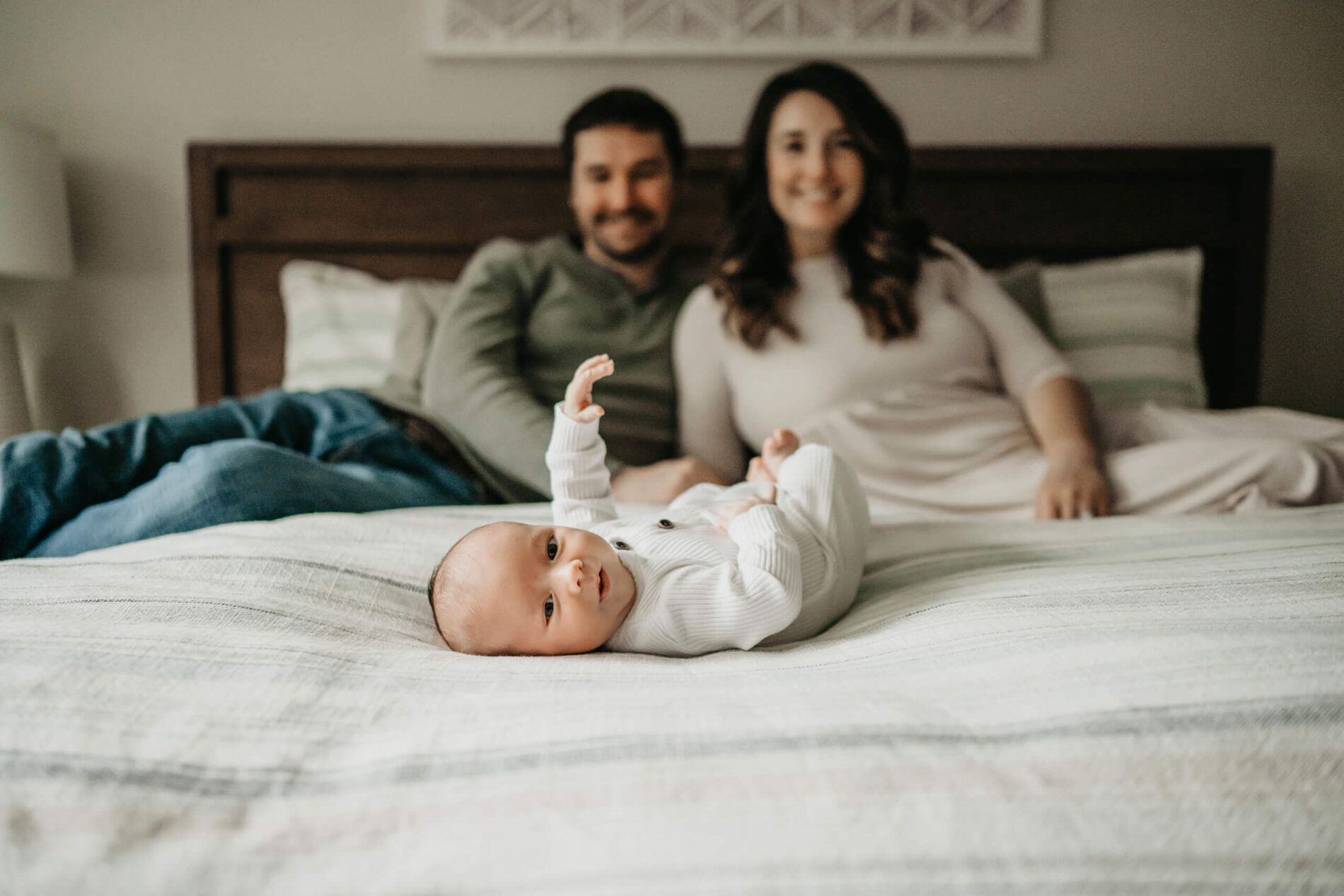 Happy awake newborn boy lying on parent's bed with mom and dad blurred in the background