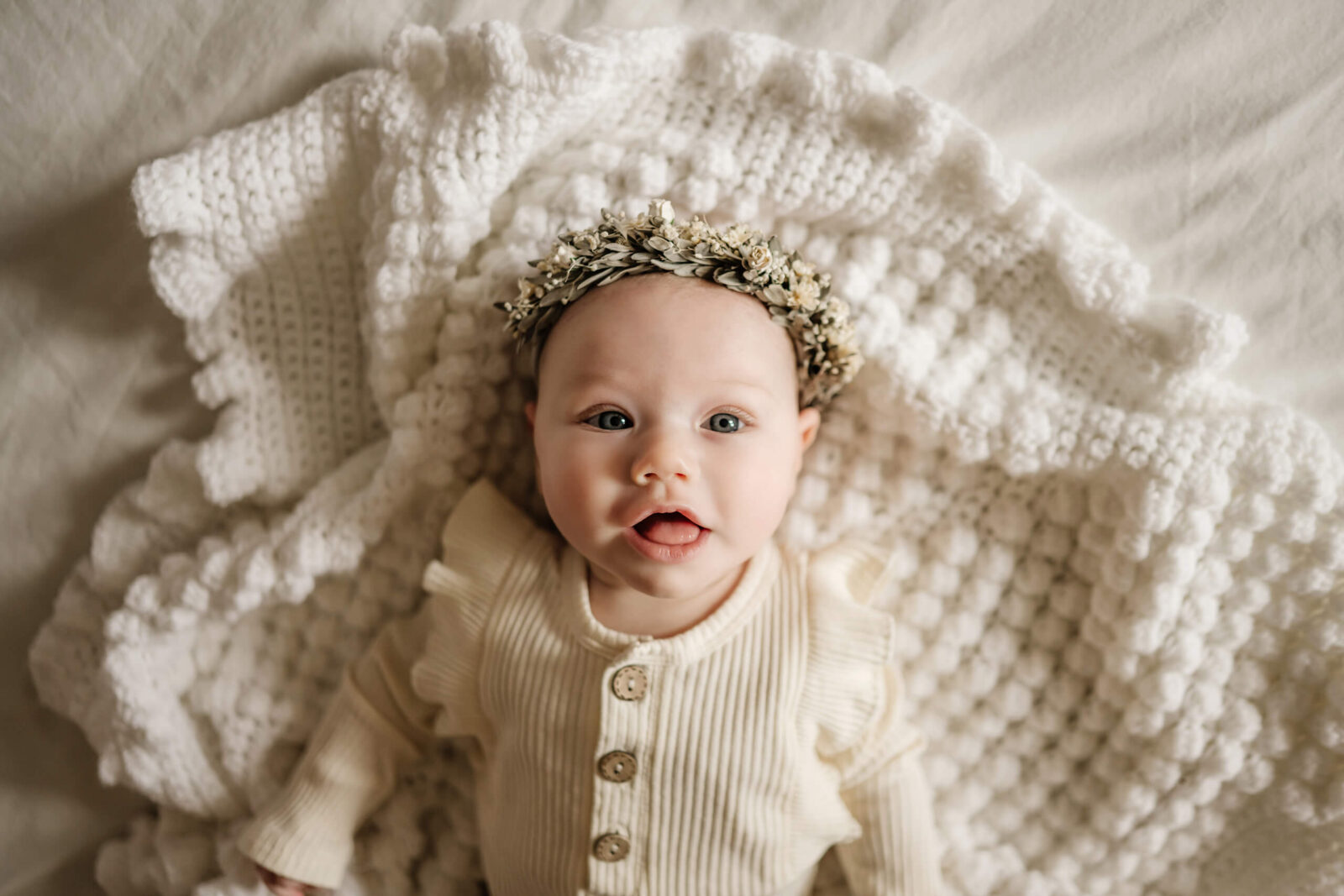 Seattle in-home newborn photo shoot, a smiling newborn girl lying in big bed on top of cozy blankets