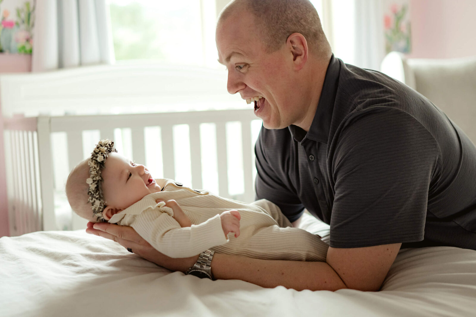 Seattle in-home newborn photo shoot, dad holding his baby girl, both smiling with a crib in the background