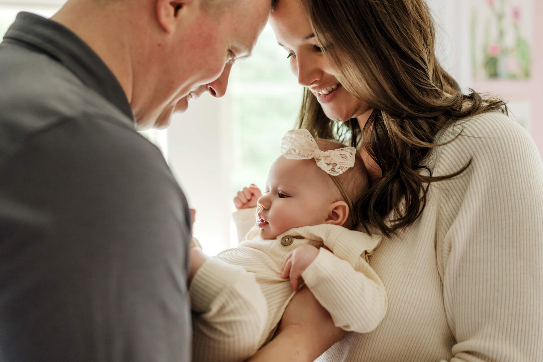 Parents standing in front of a window, holding their baby girl between them, all smiling