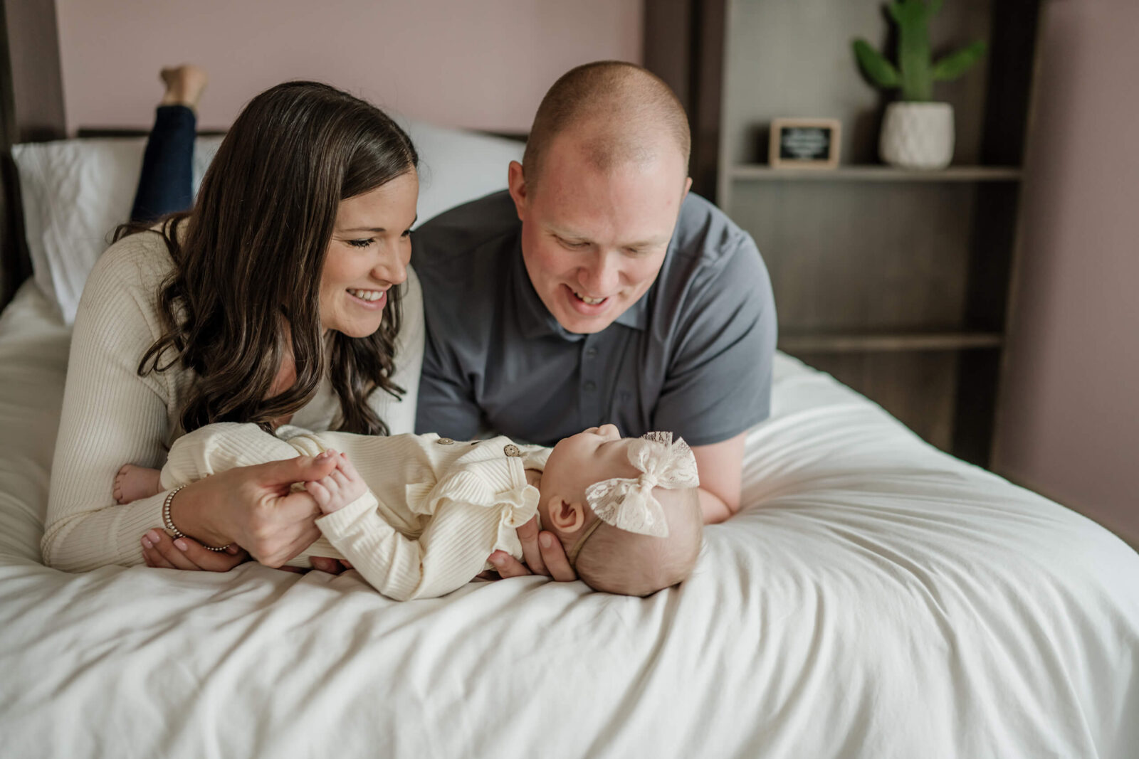 Seattle in-home newborn photo shoot, mom and dad lying on their bed with their baby girl in front of them, all smiling